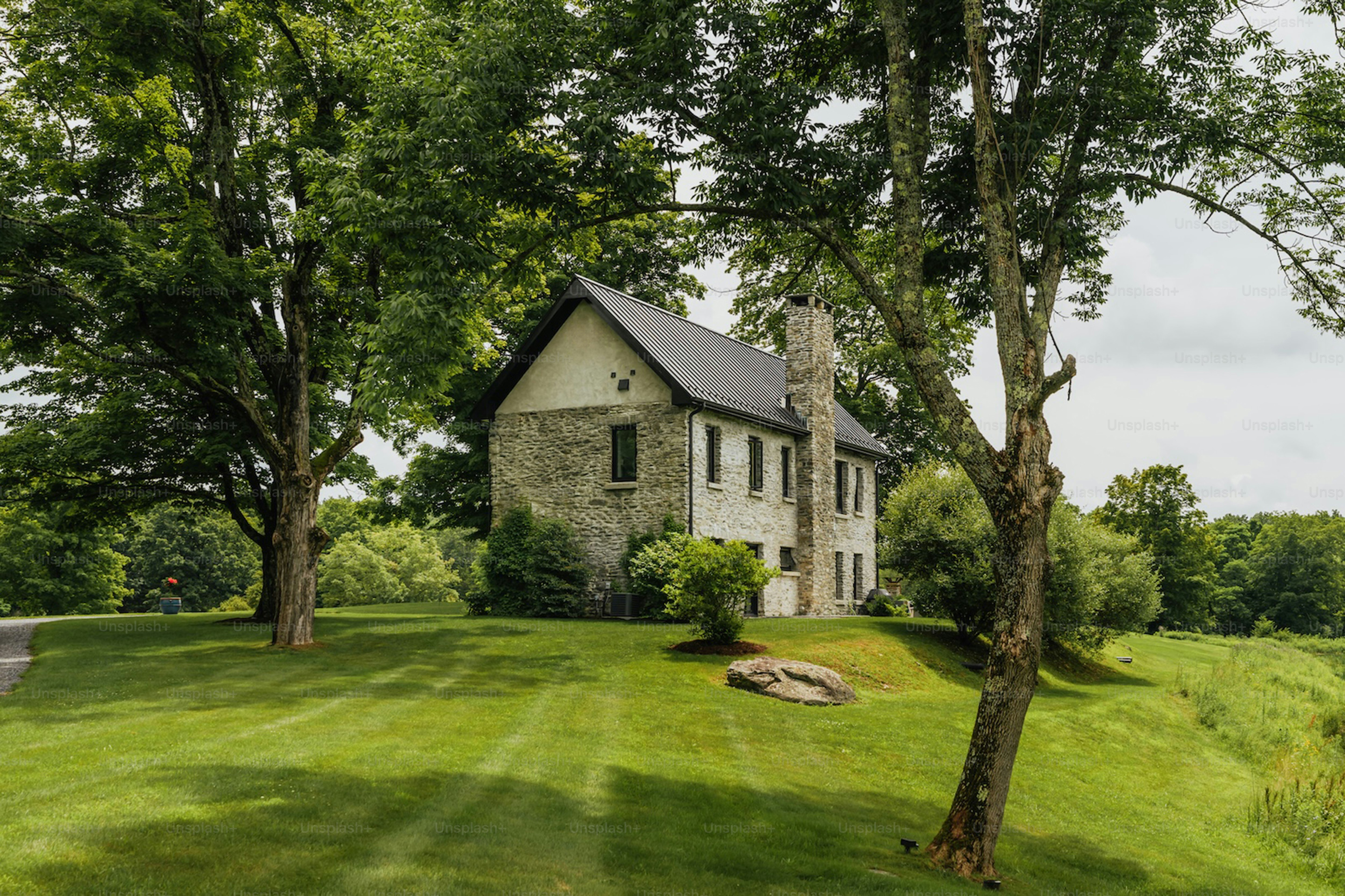 Stone house with a chimney surrounded by green trees.