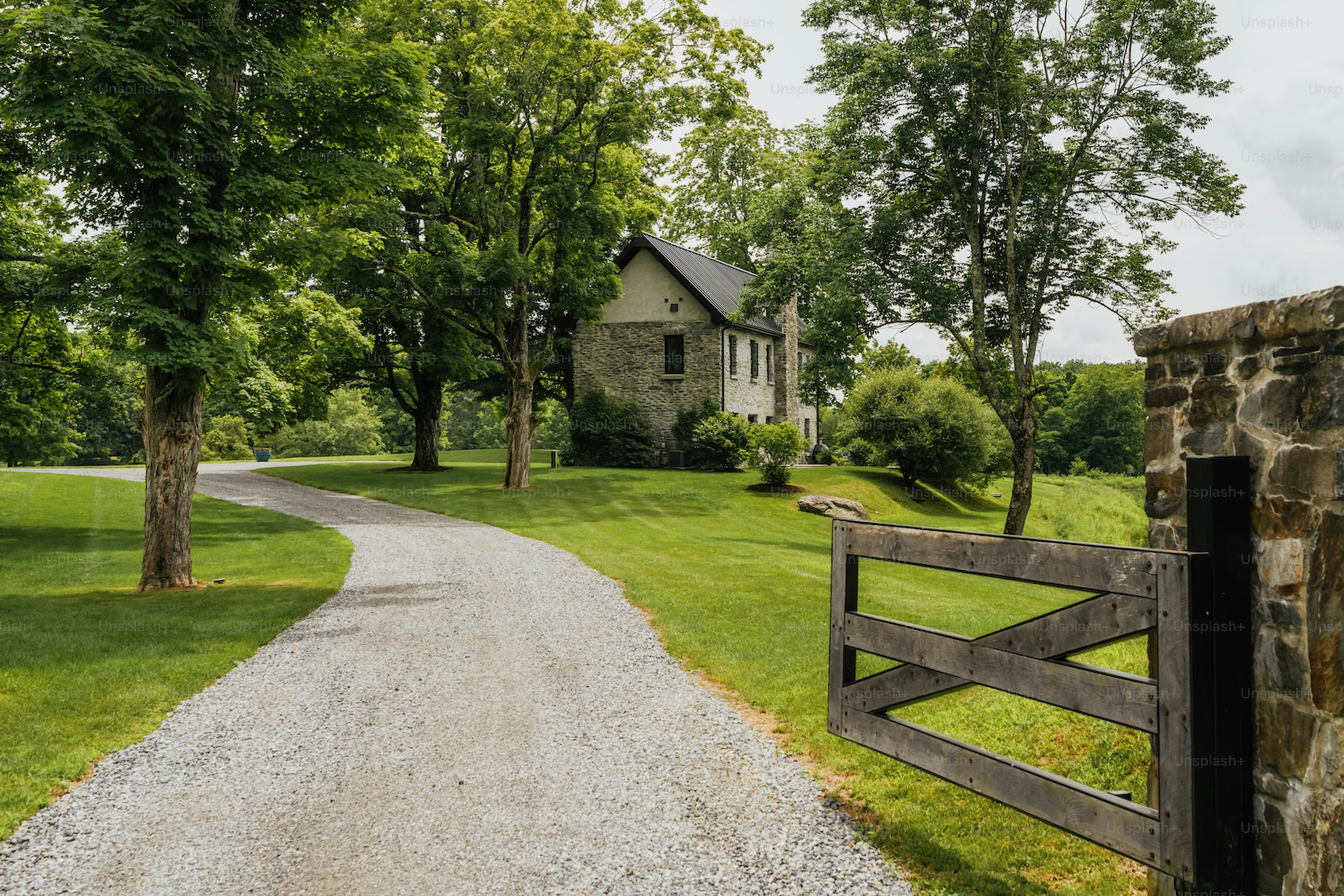 Gravel driveway leads to stone house with gate