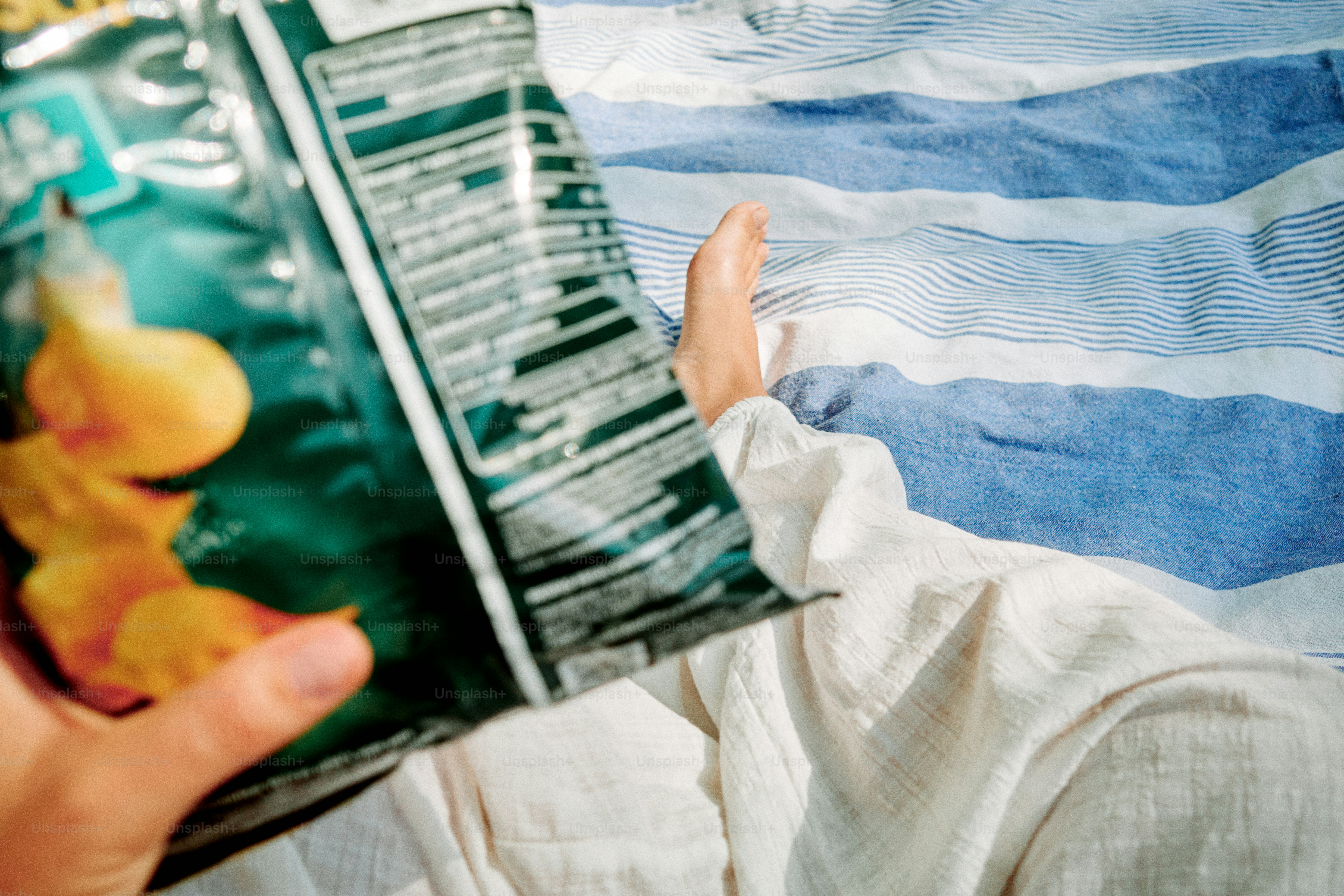 Person holding bag of chips on striped blanket