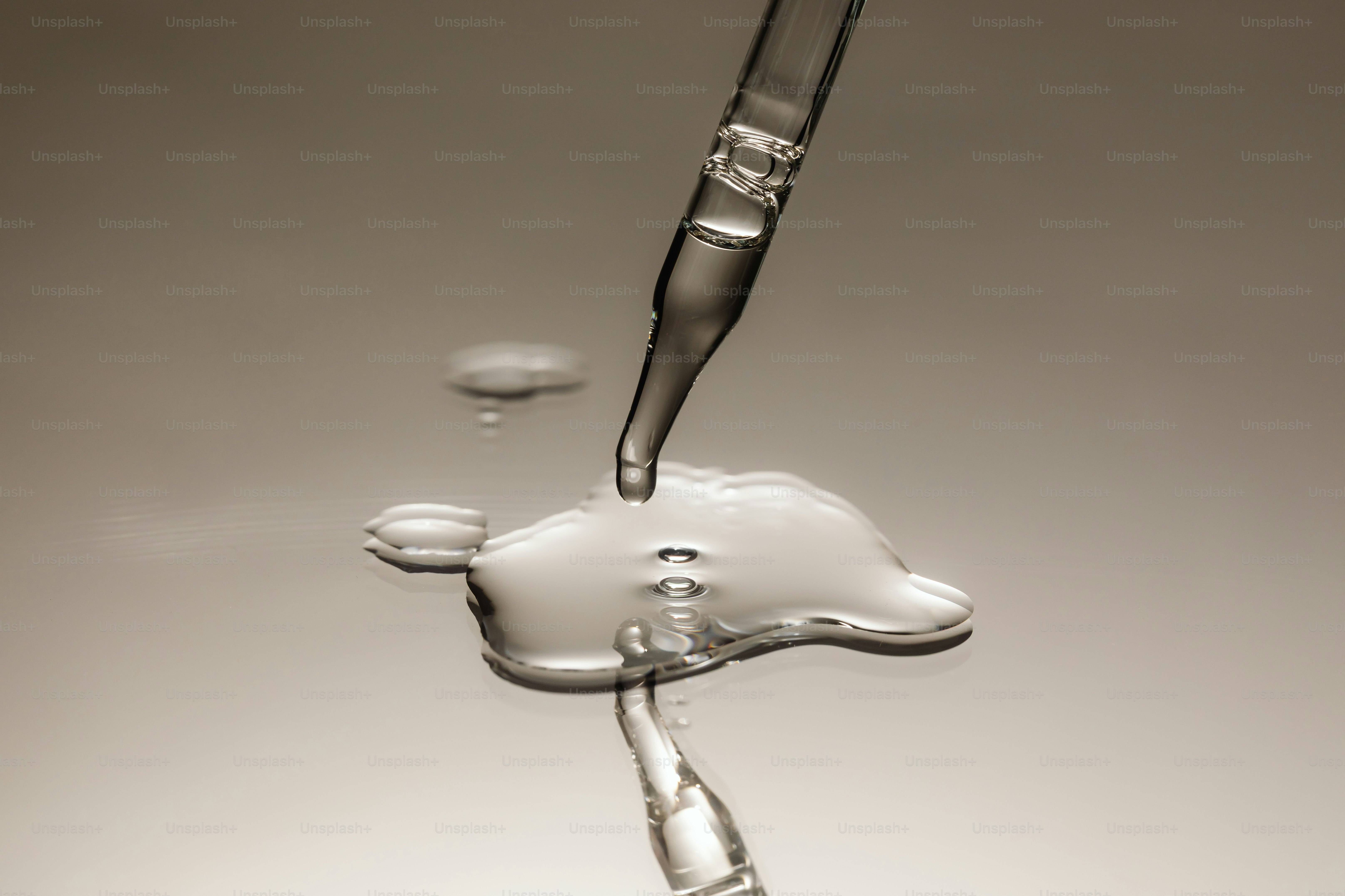 A pipette dripping liquid onto a reflective surface. photo – Macro ...