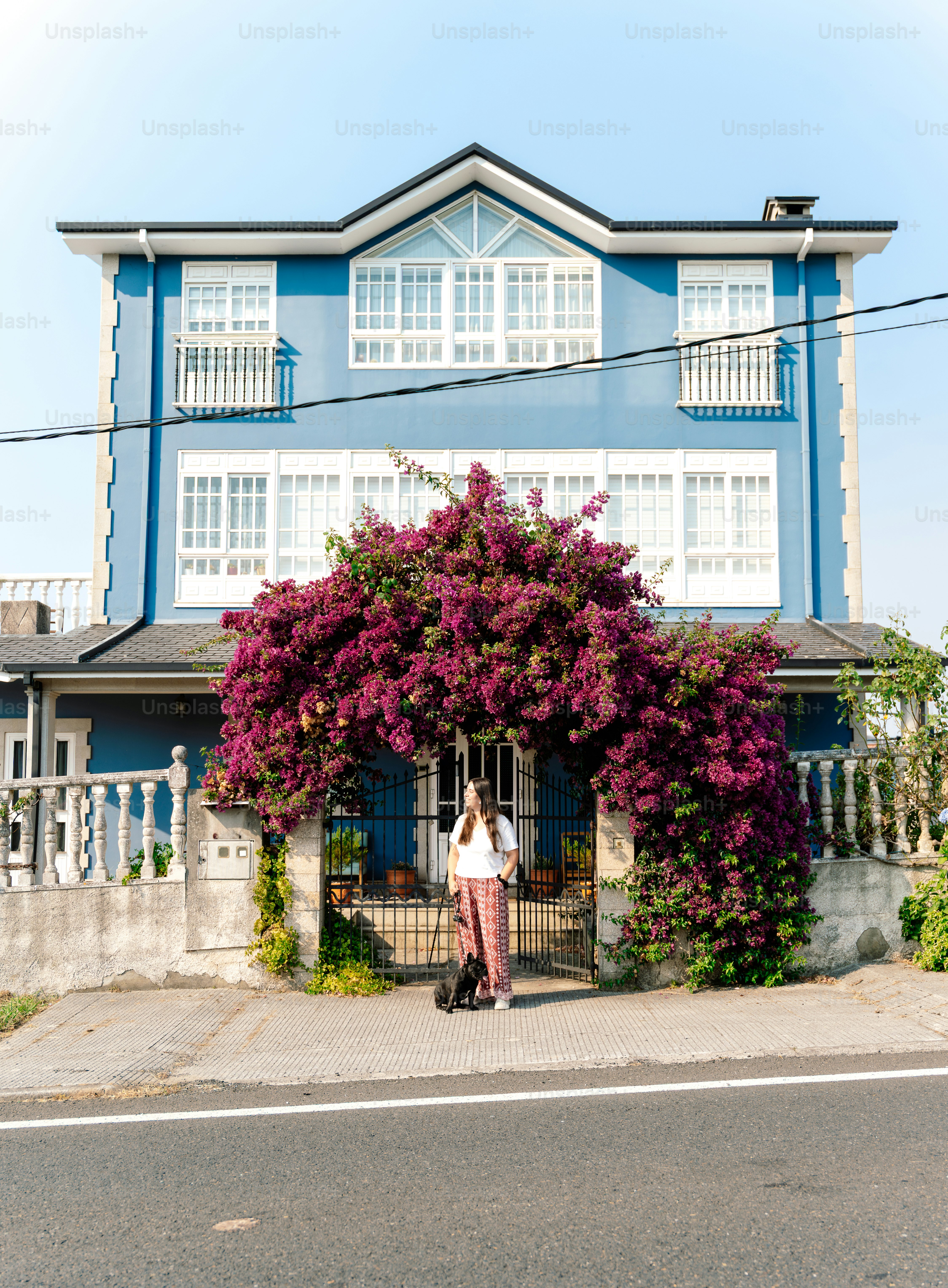 Woman with dog in front of blue house with flowers.