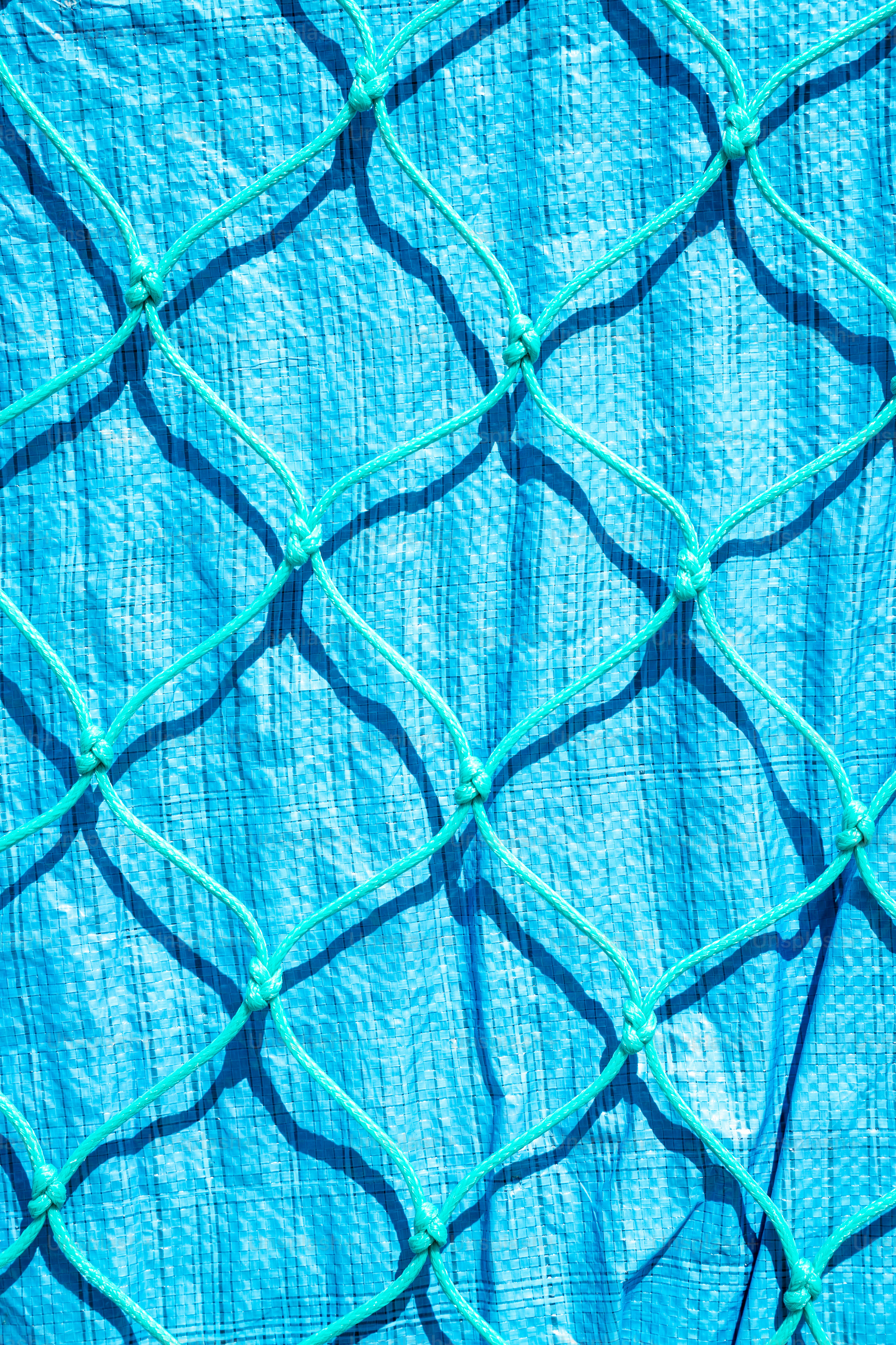 Ein türkisfarbenes Netz wirft Schatten auf eine blaue Plane.
