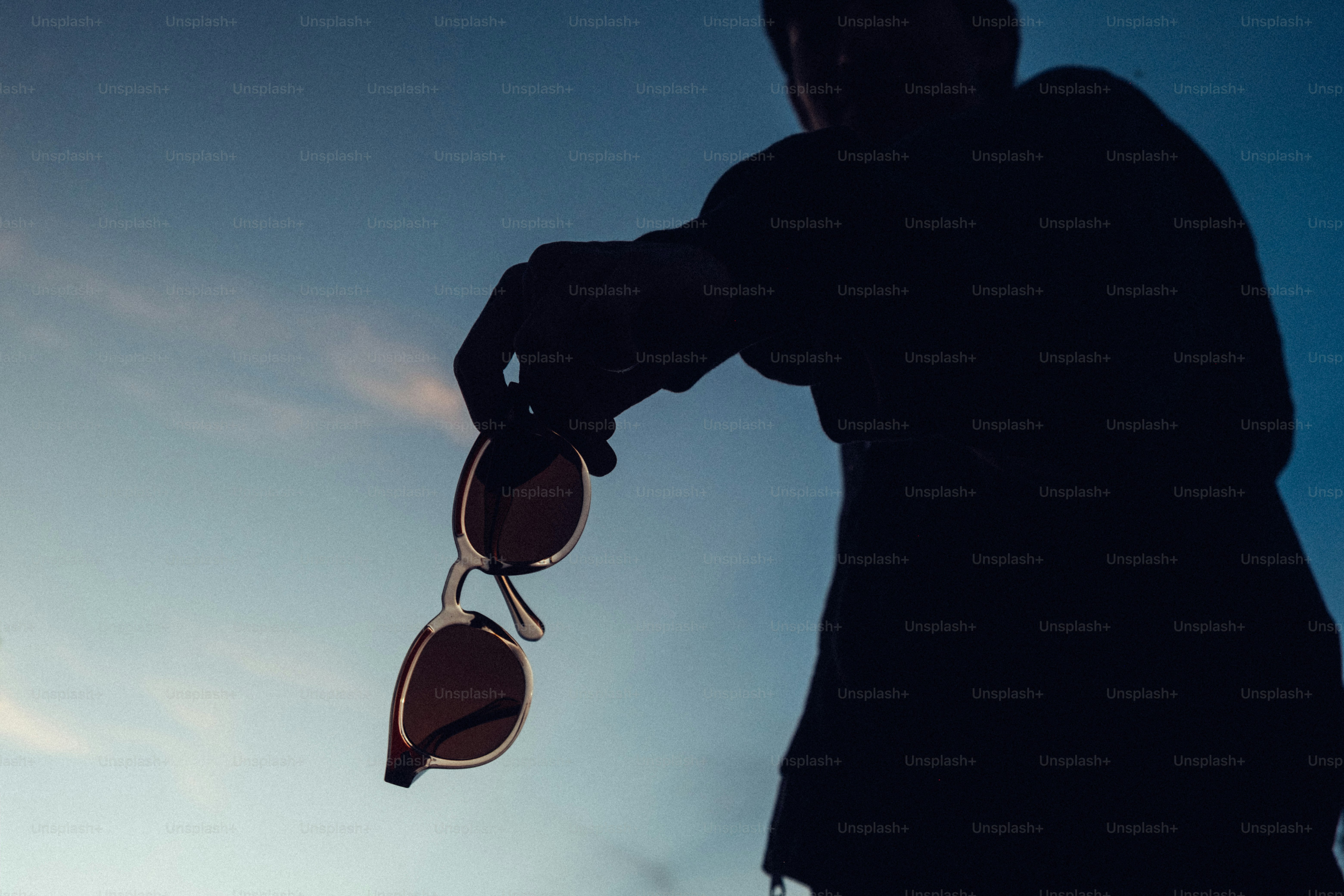 Man holding sunglasses against a twilight sky photo – Vision Image on ...