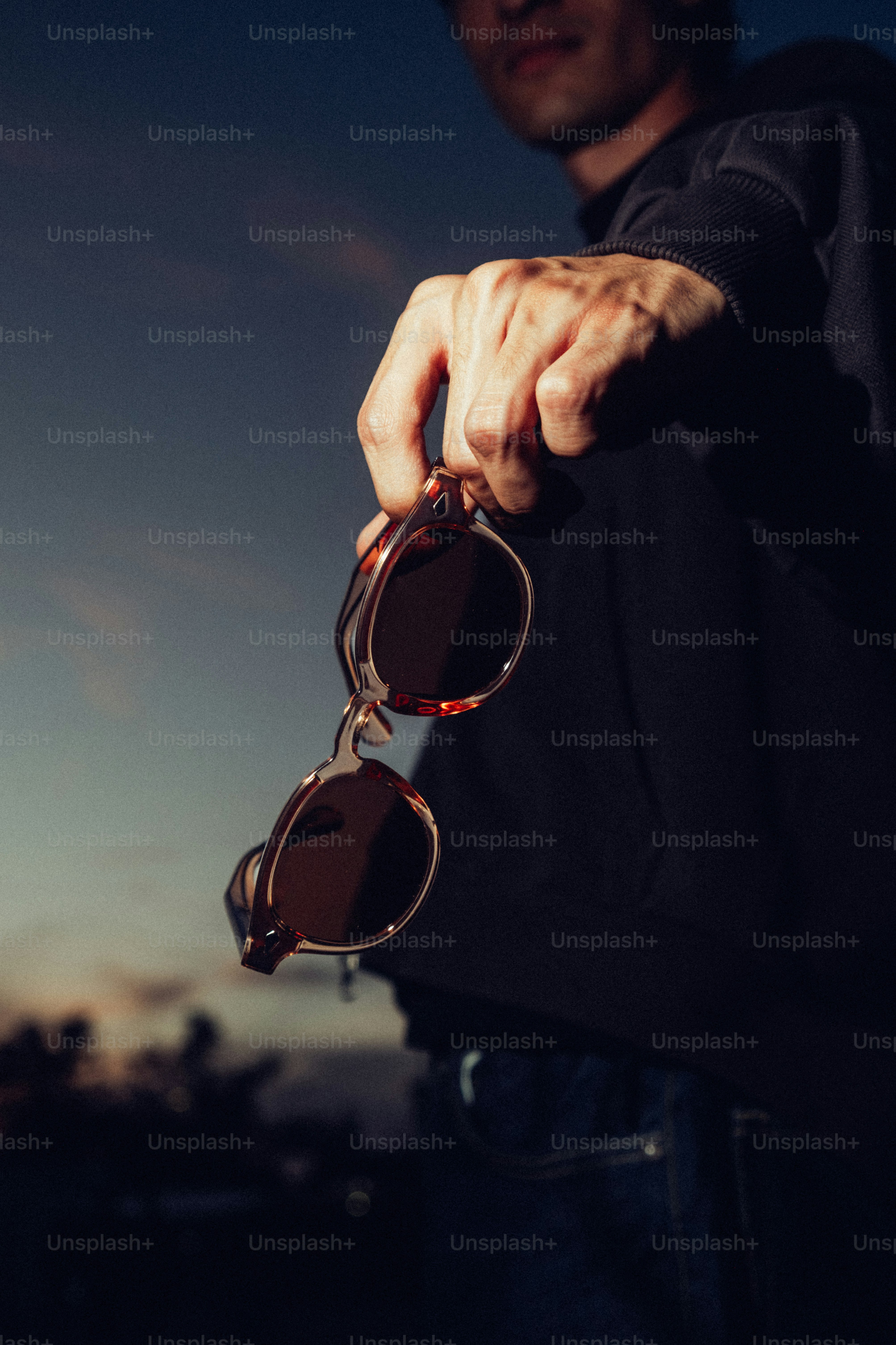 Man holding sunglasses against a twilight sky photo – Vision Image on ...
