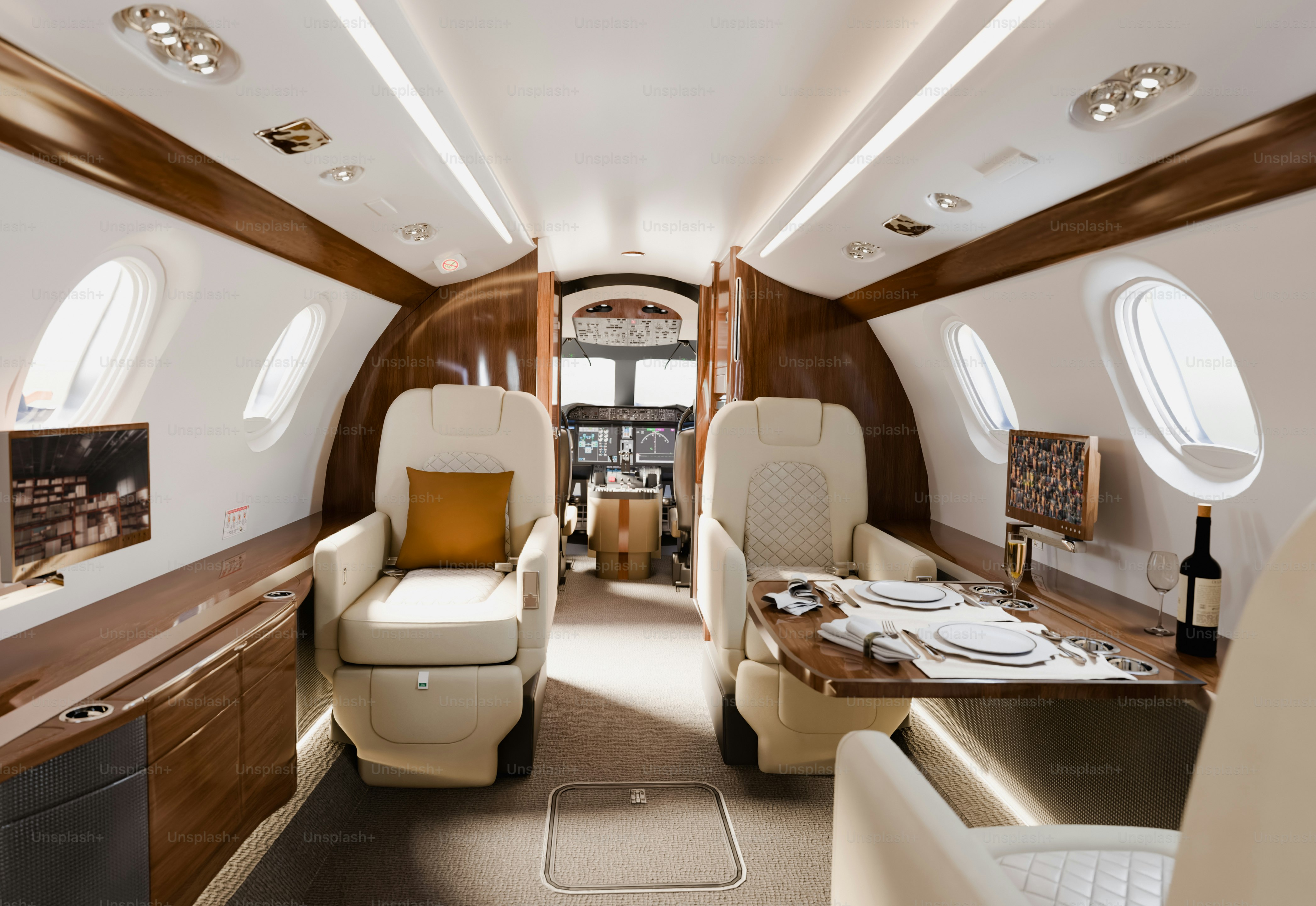 Interior of a luxurious private jet featuring plush seats, a dining table set for a meal, wooden accents, and large windows.