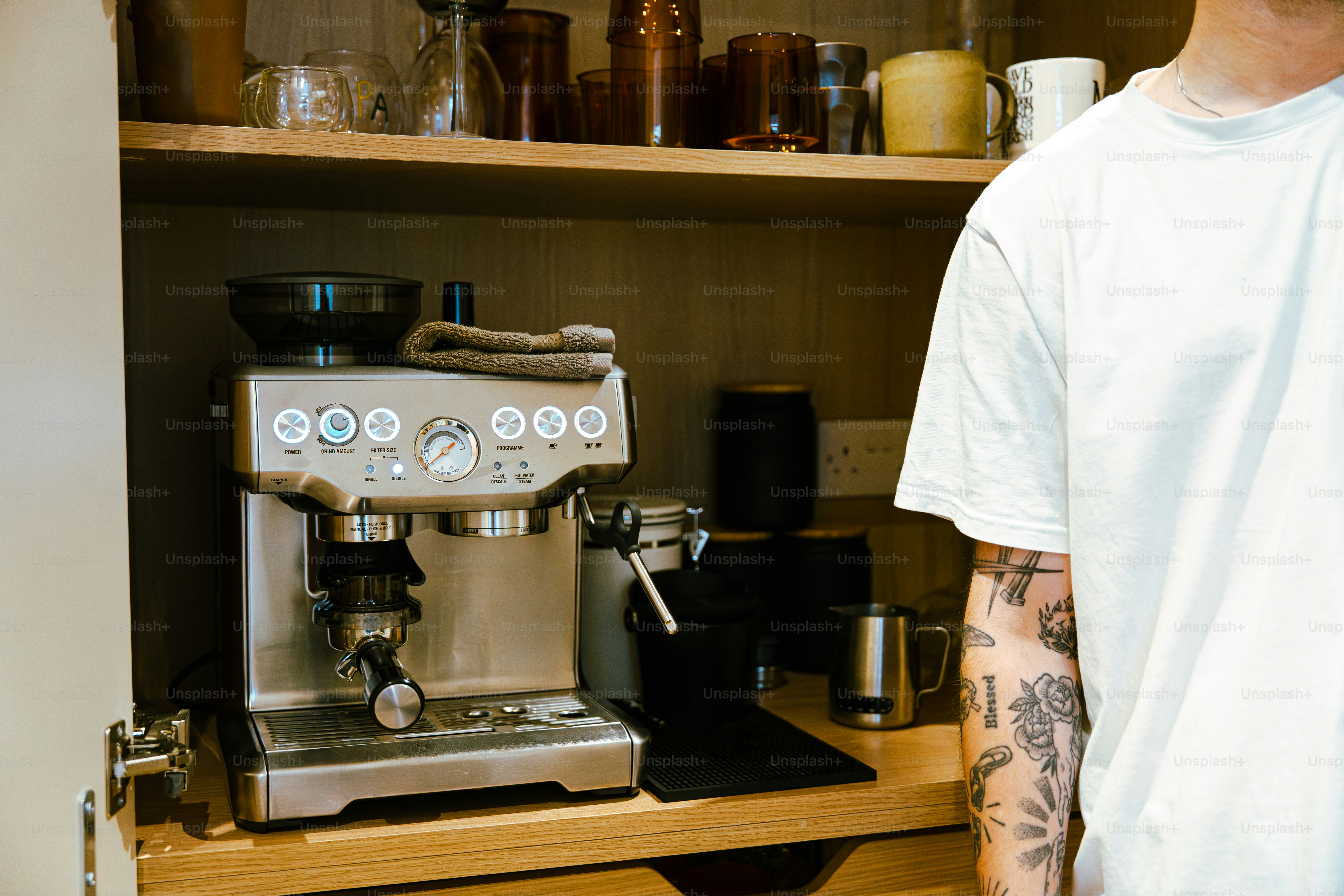 Man with tattooed arm stands by espresso machine
