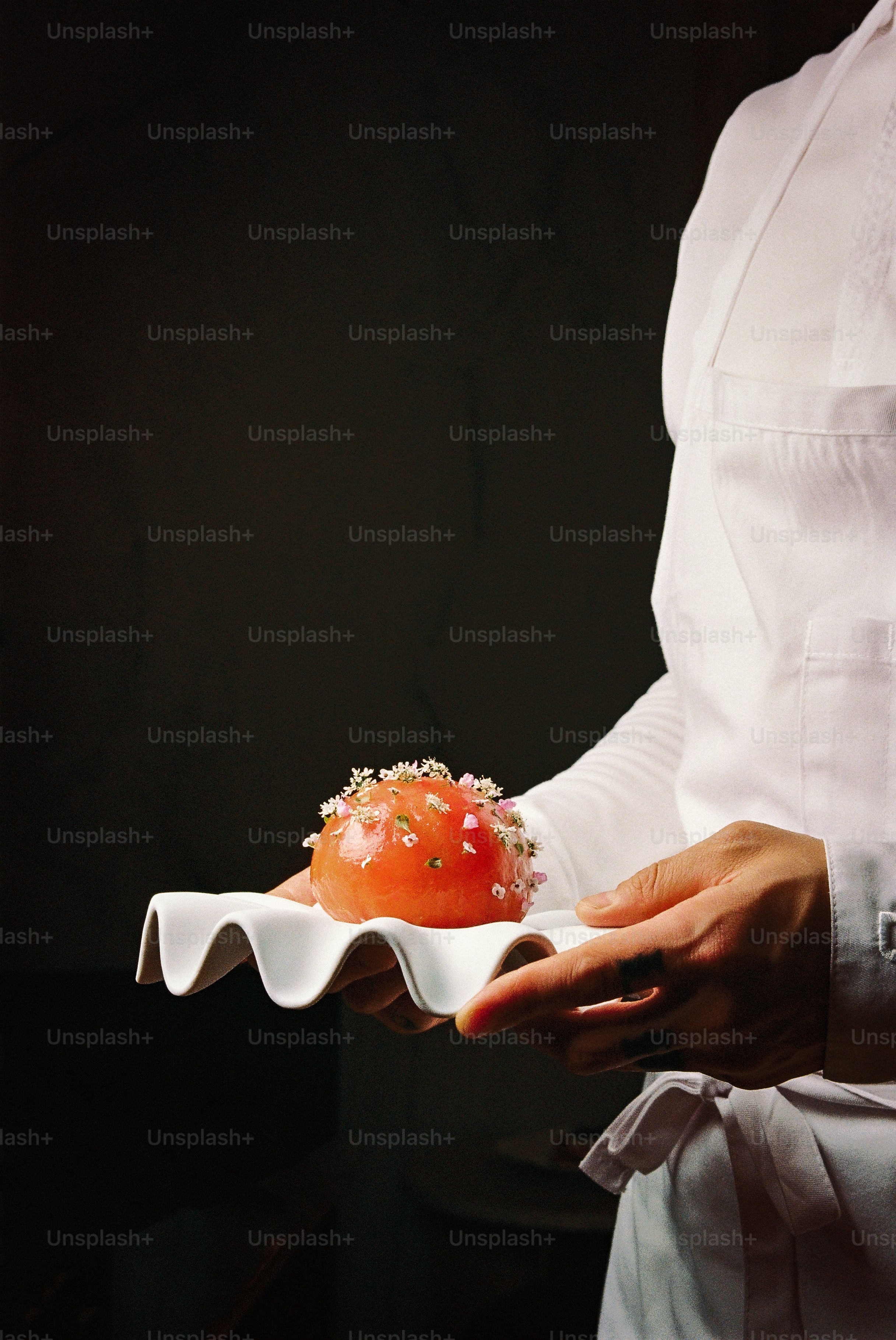 Chef presents a delicate dessert on a white wavy plate.
