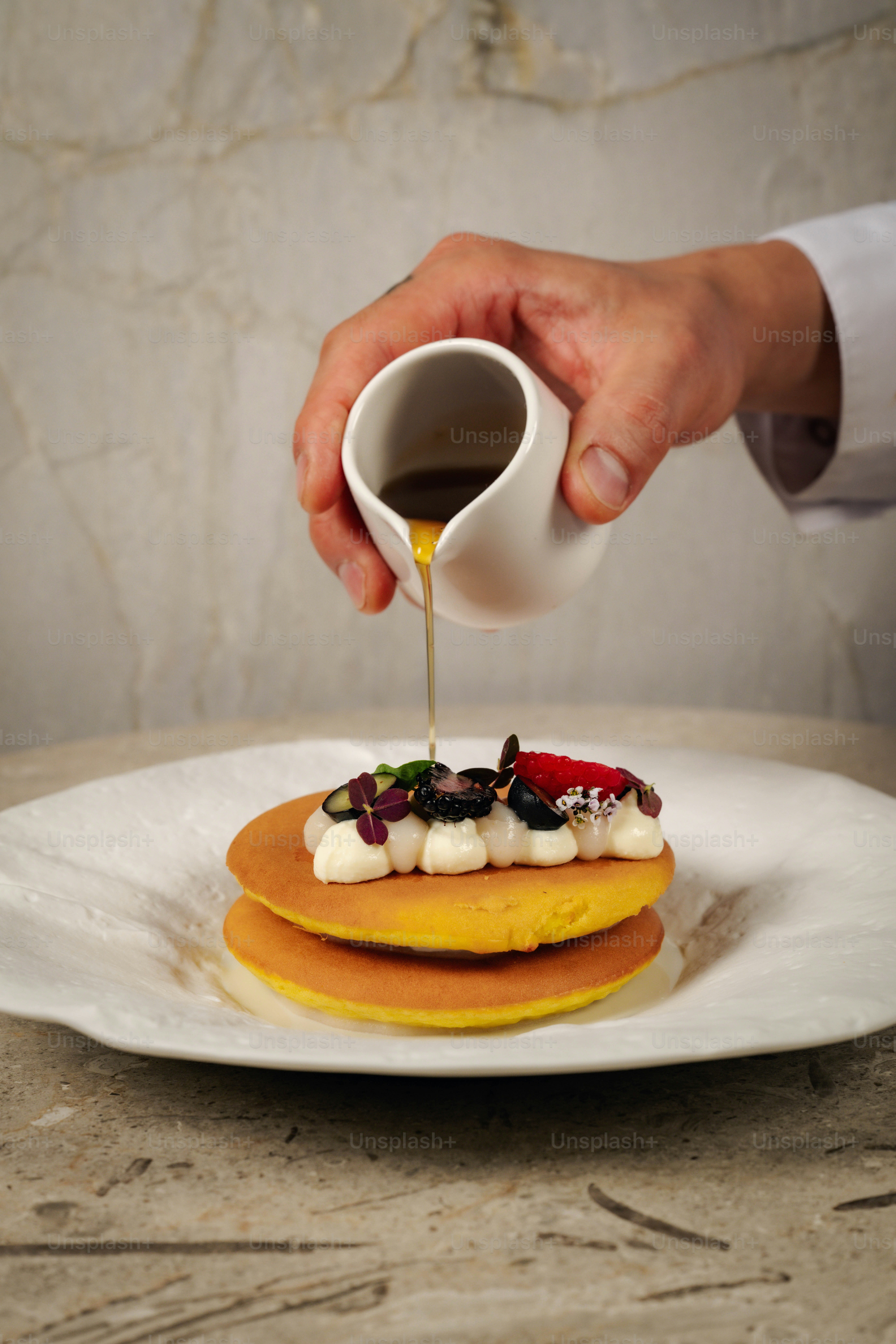 Le chef verse du sirop sur des crêpes empilées avec des garnitures.