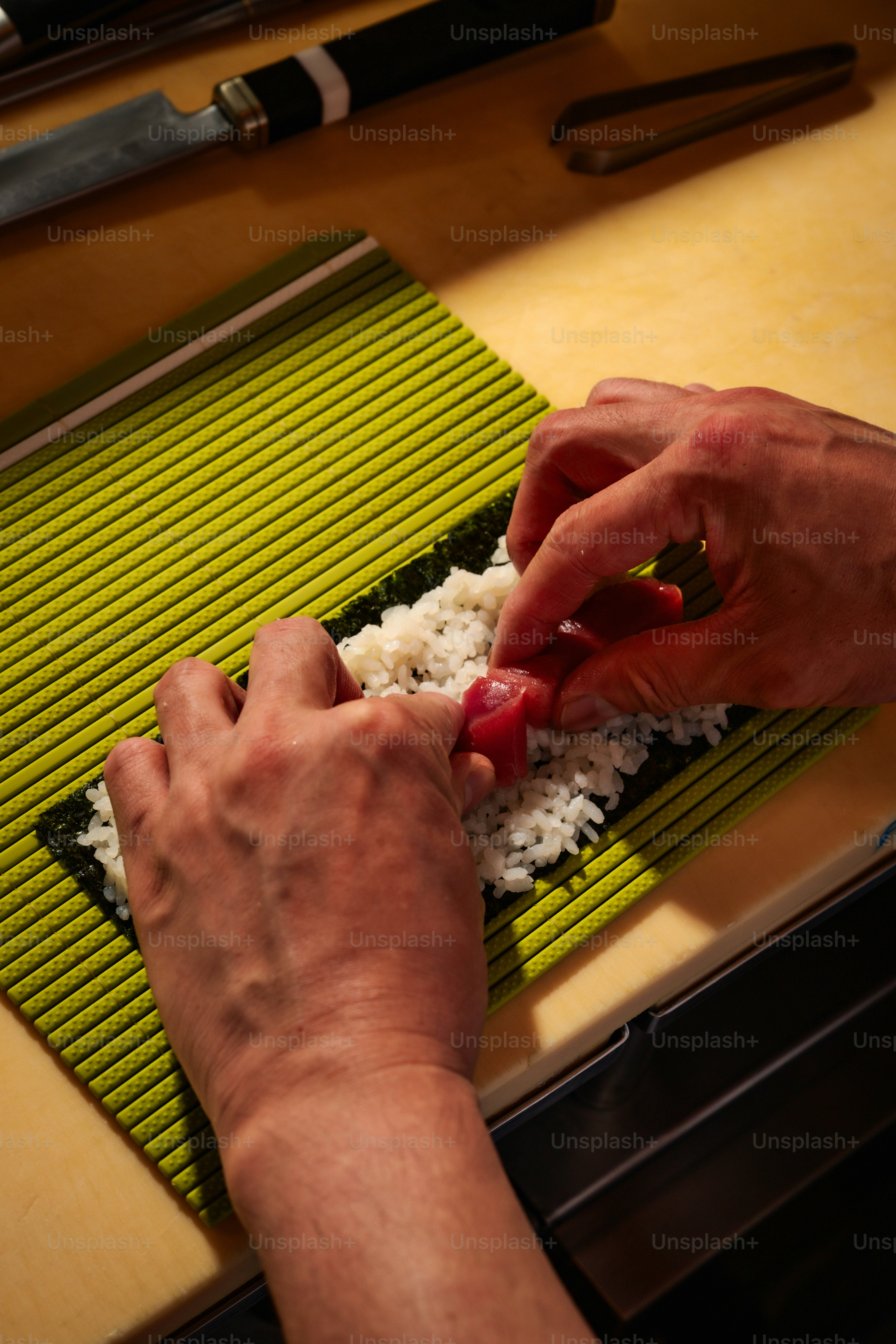 Chef prepares sushi with rice and tuna on seaweed.