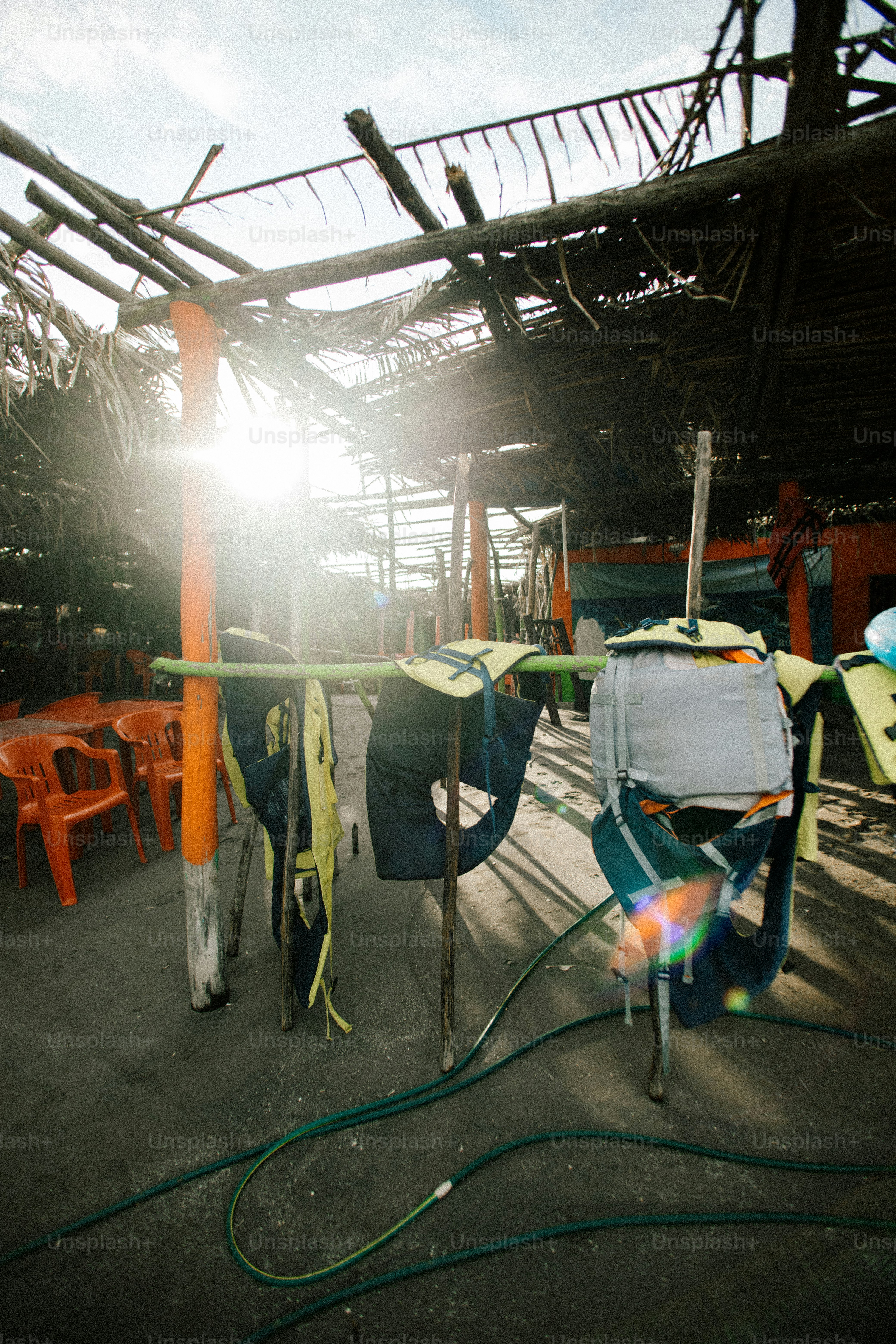 Life jackets hang on a rack under a thatched roof.