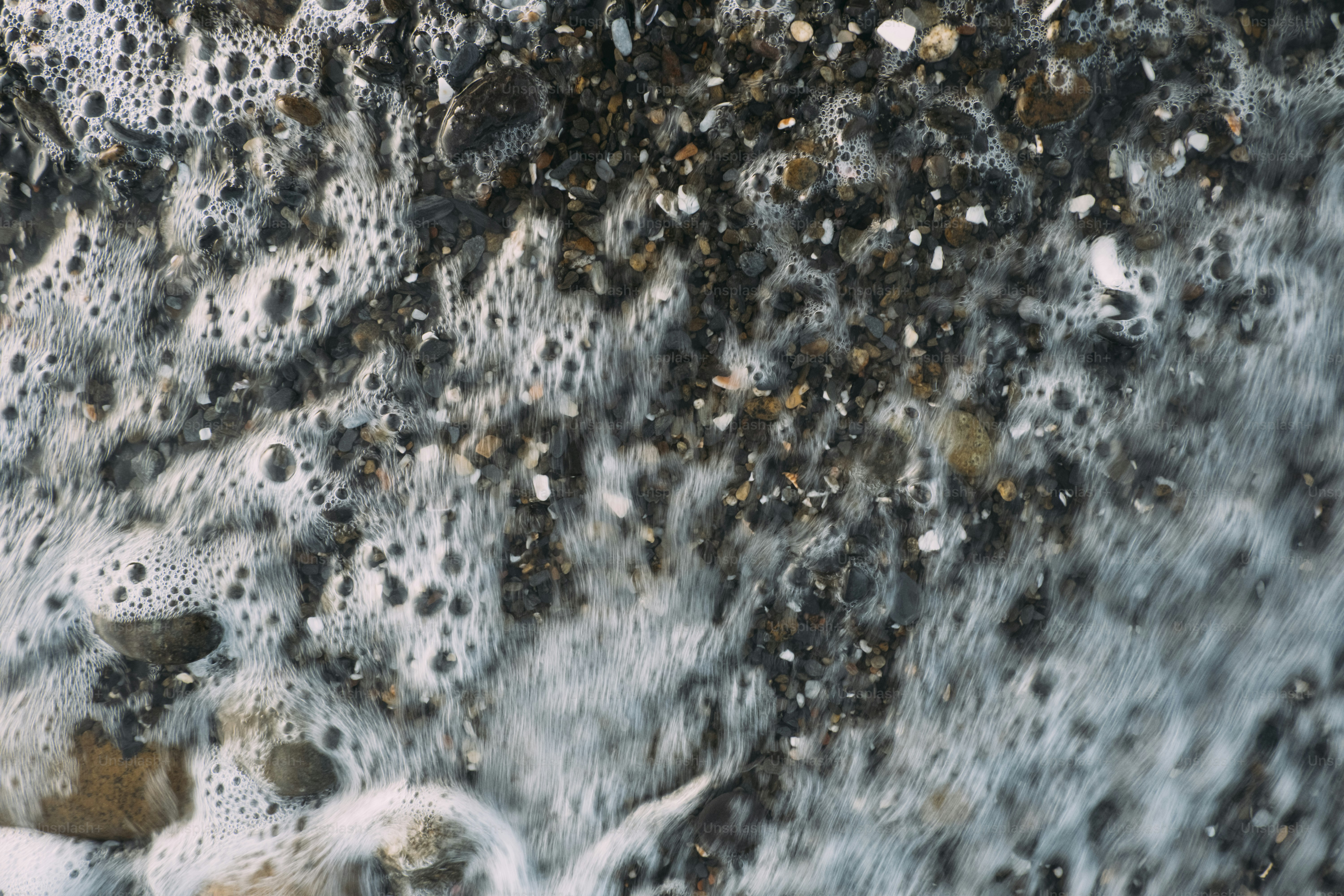 Água espumosa lava seixos em uma praia.