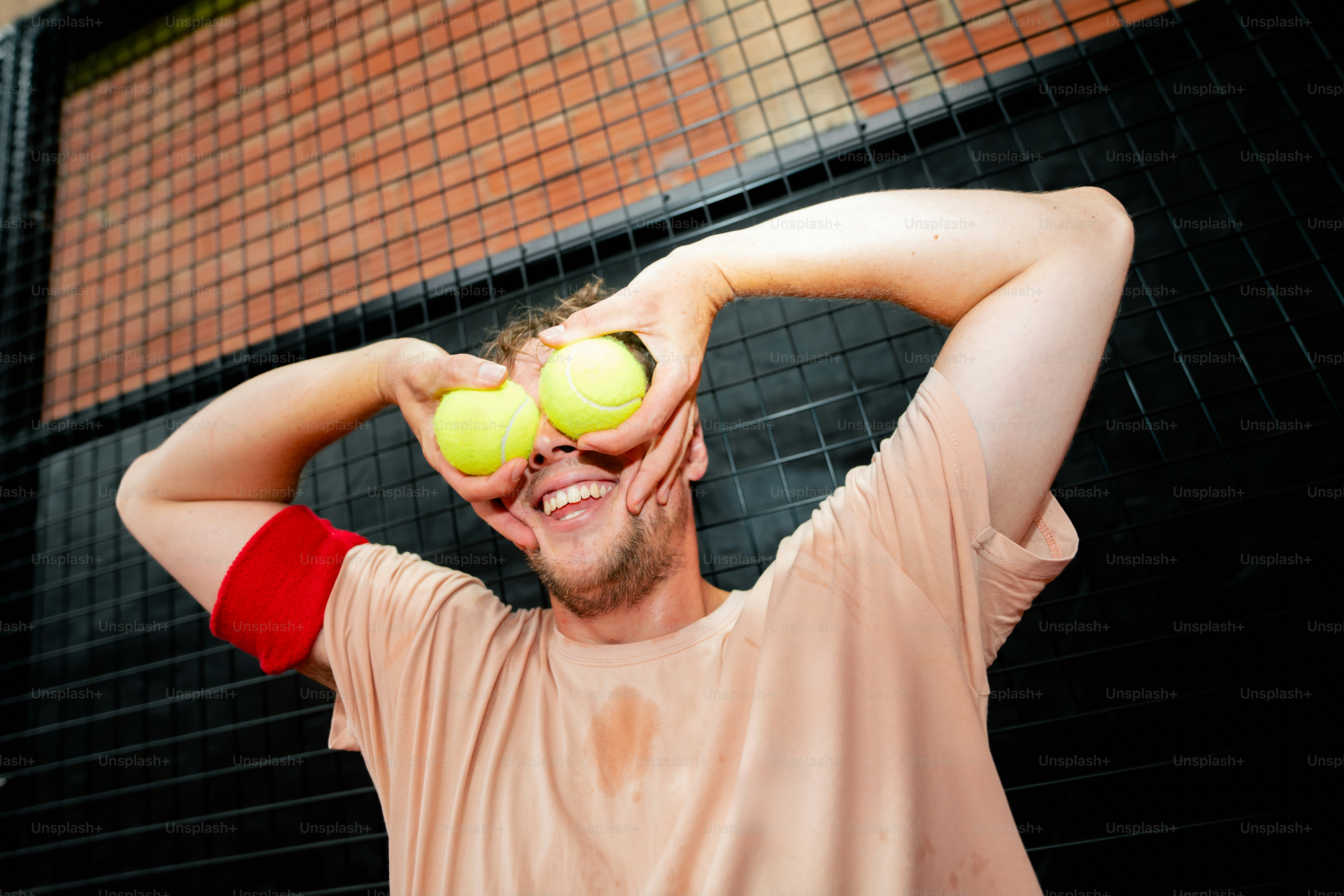 Mann hält sich lächelnd Tennisbälle über die Augen.