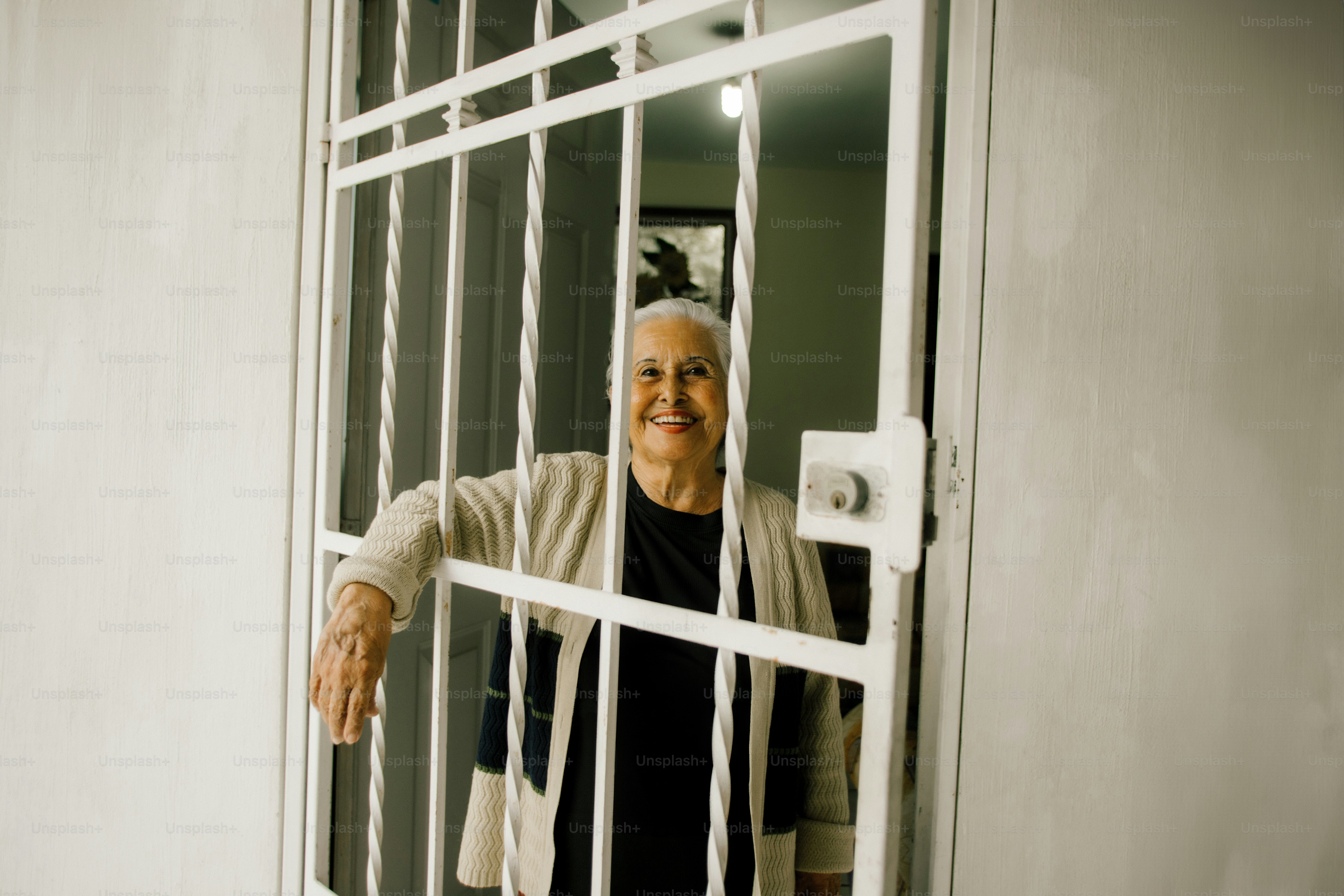 Elderly woman smiling behind a white metal gate.
