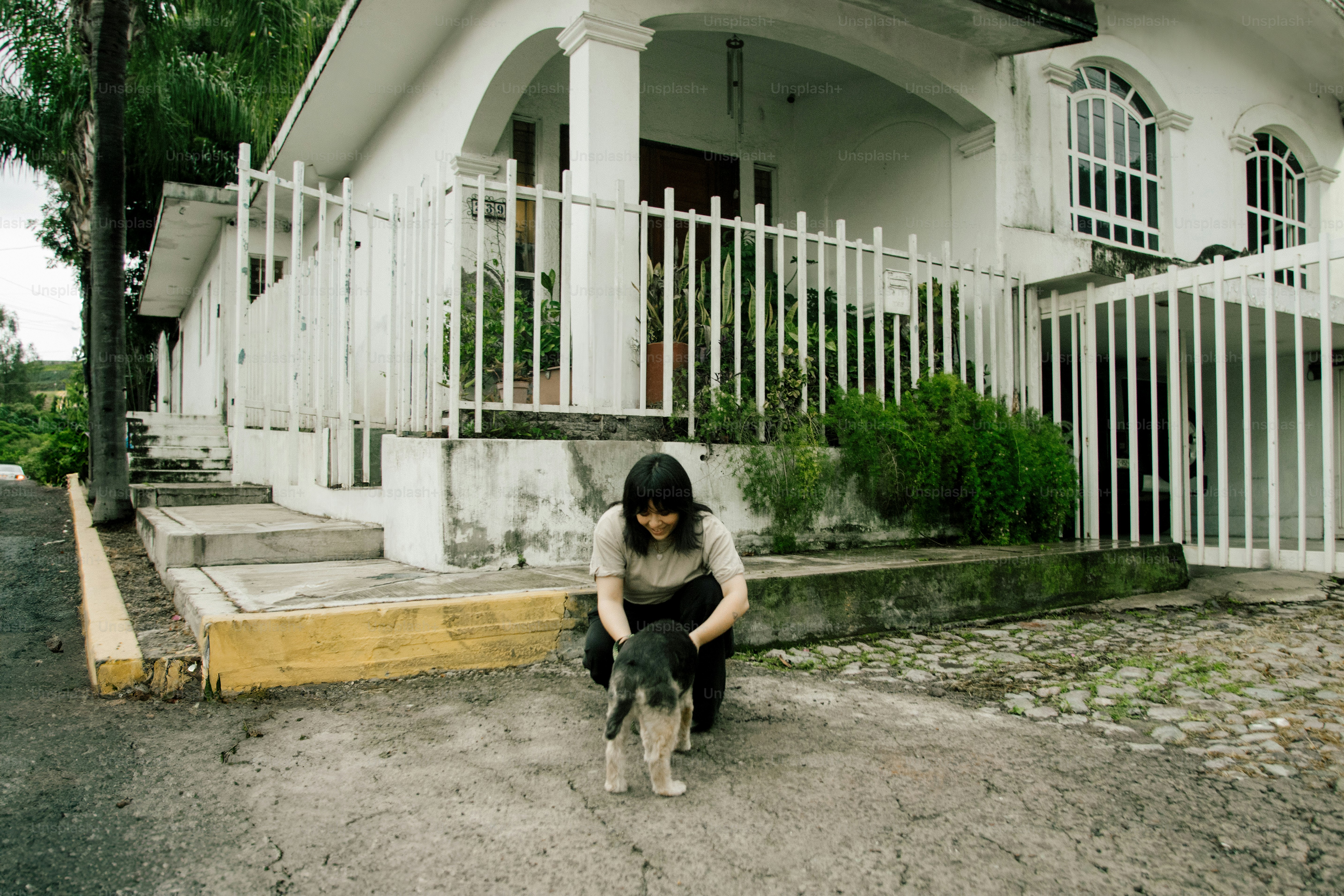 Woman petting a small dog in front of a white house