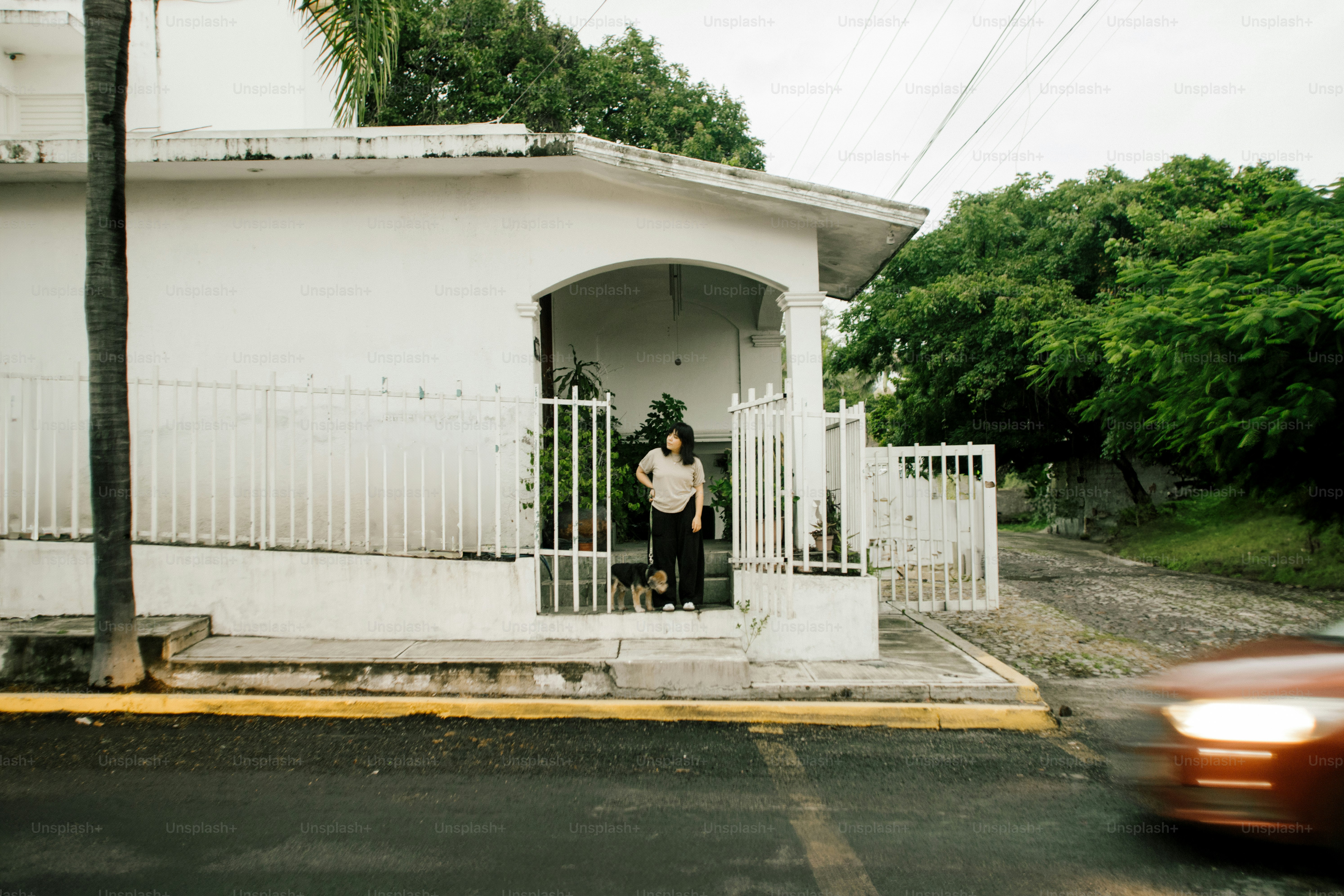 Woman and dog stand on porch of white house.