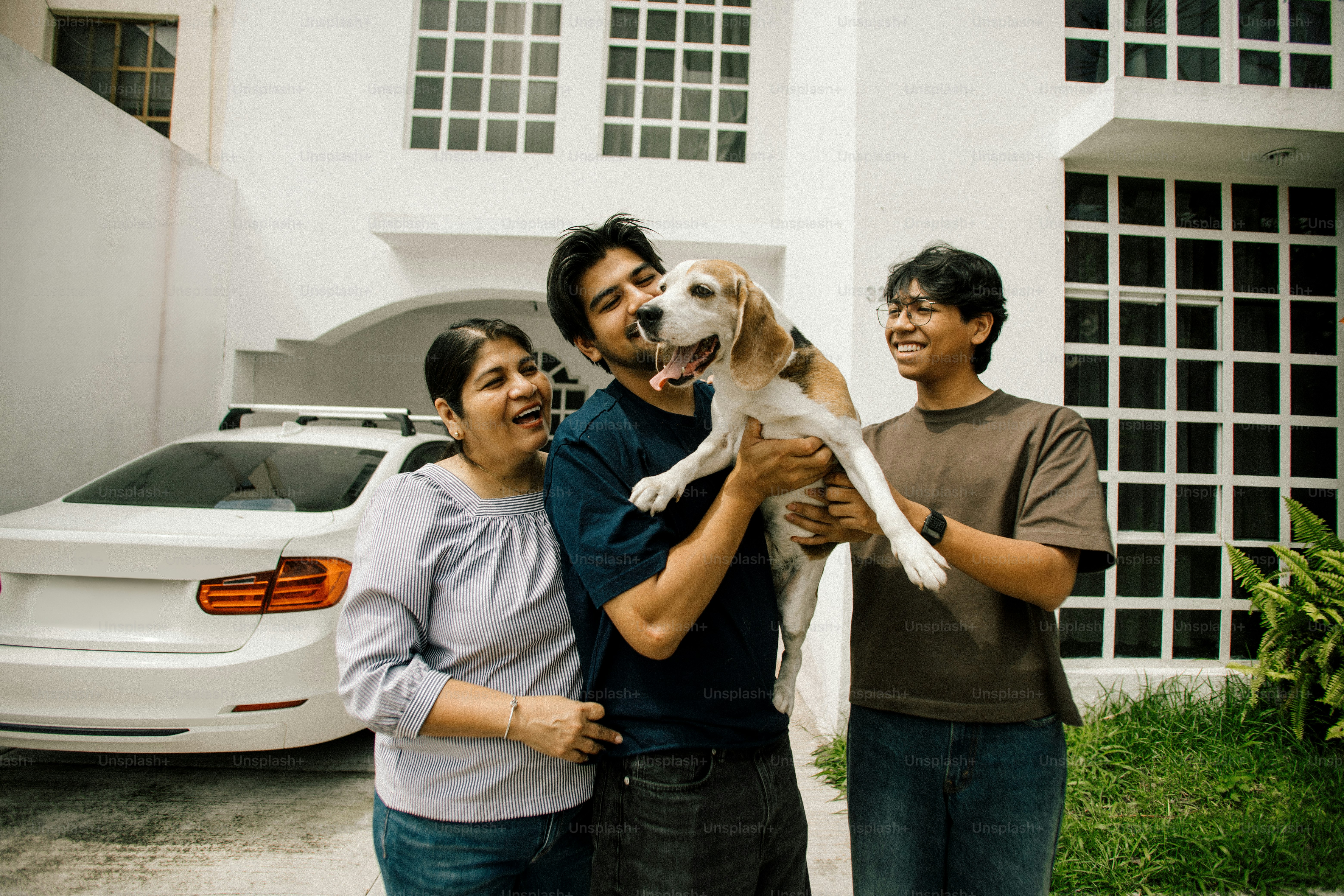 Family holding a beagle dog outside a modern house