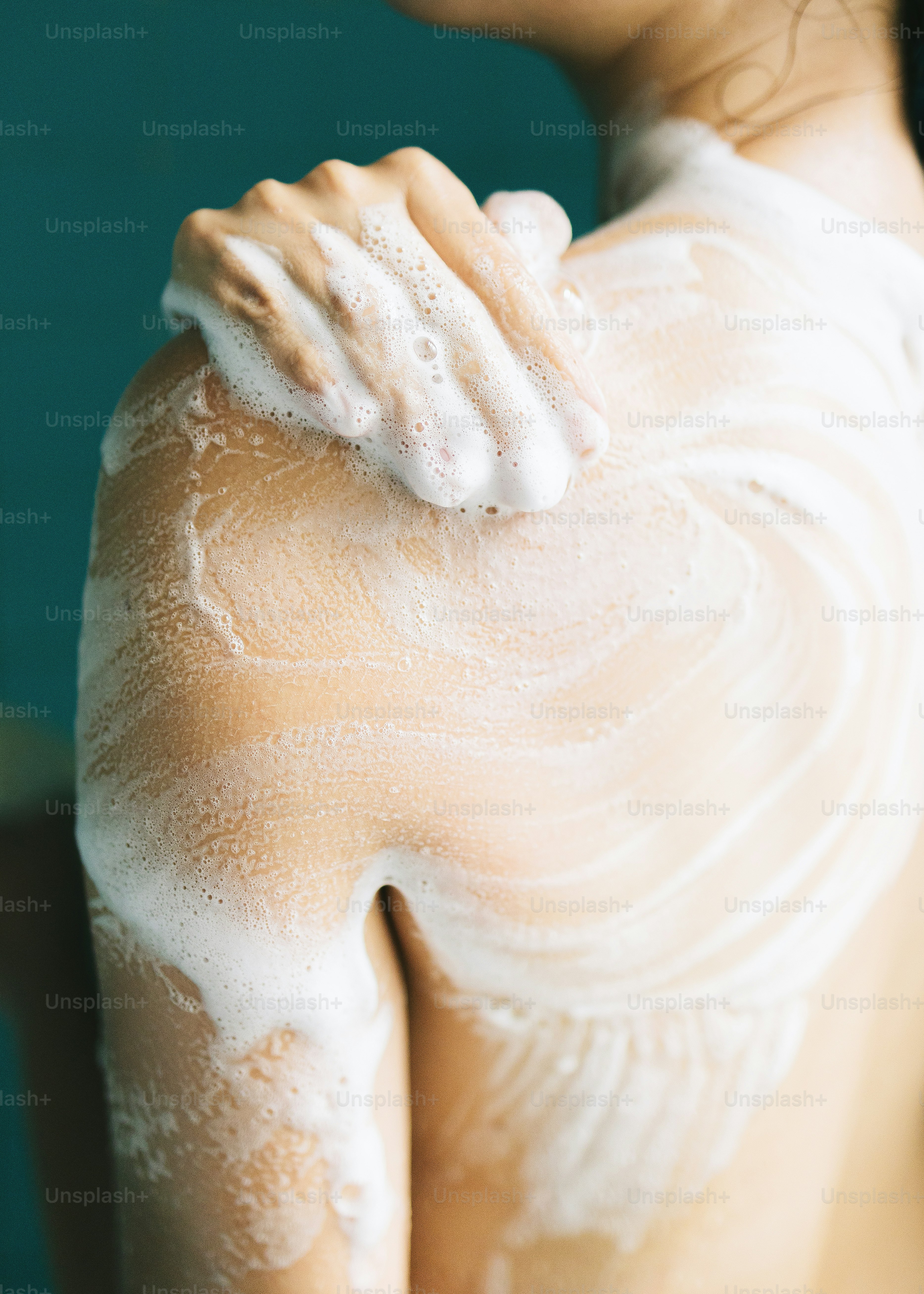 Nahaufnahme einer Person, die ihre Schulter mit Seife wäscht.