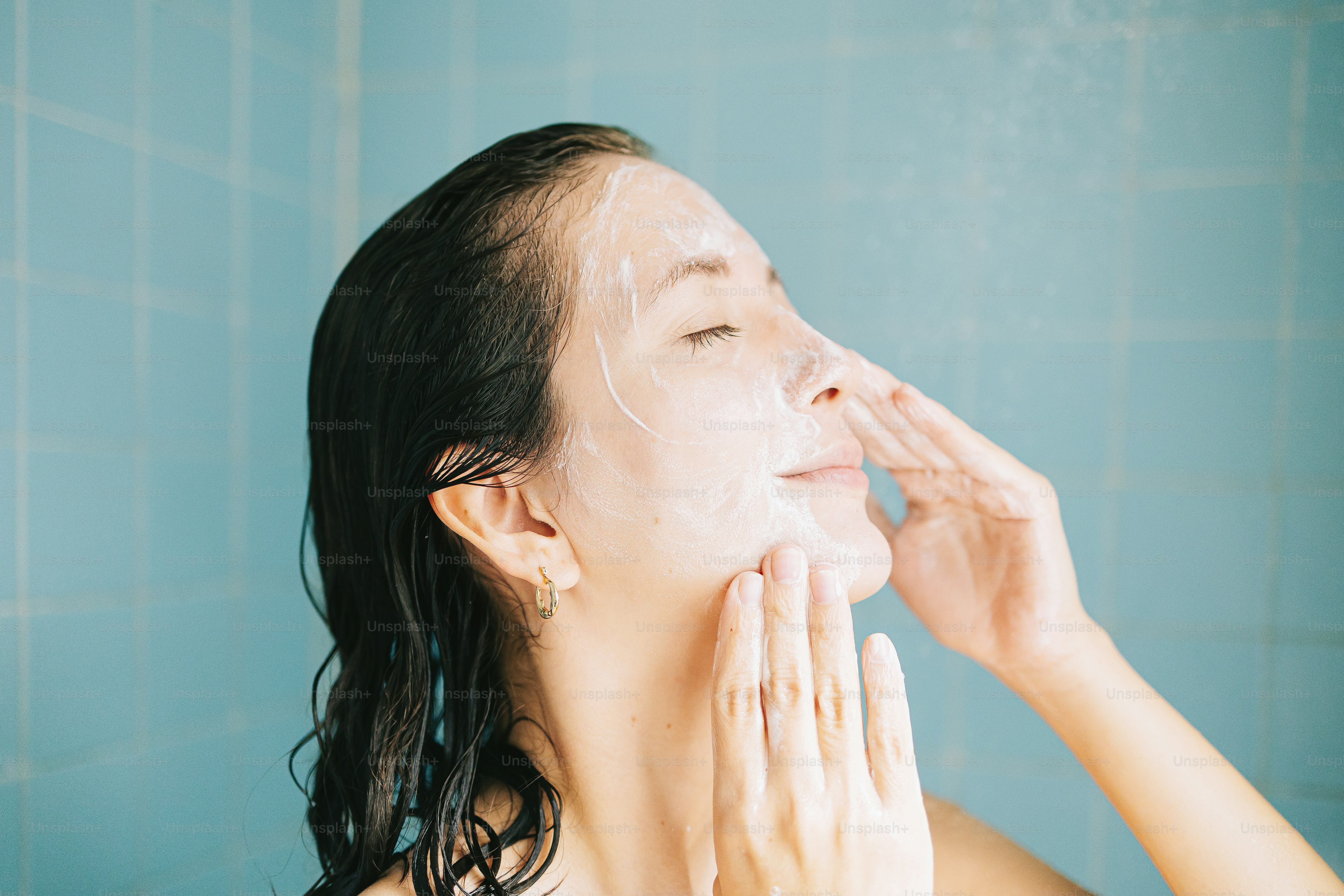 Frau, die ihr Gesicht in der Dusche mit Schaum wäscht
