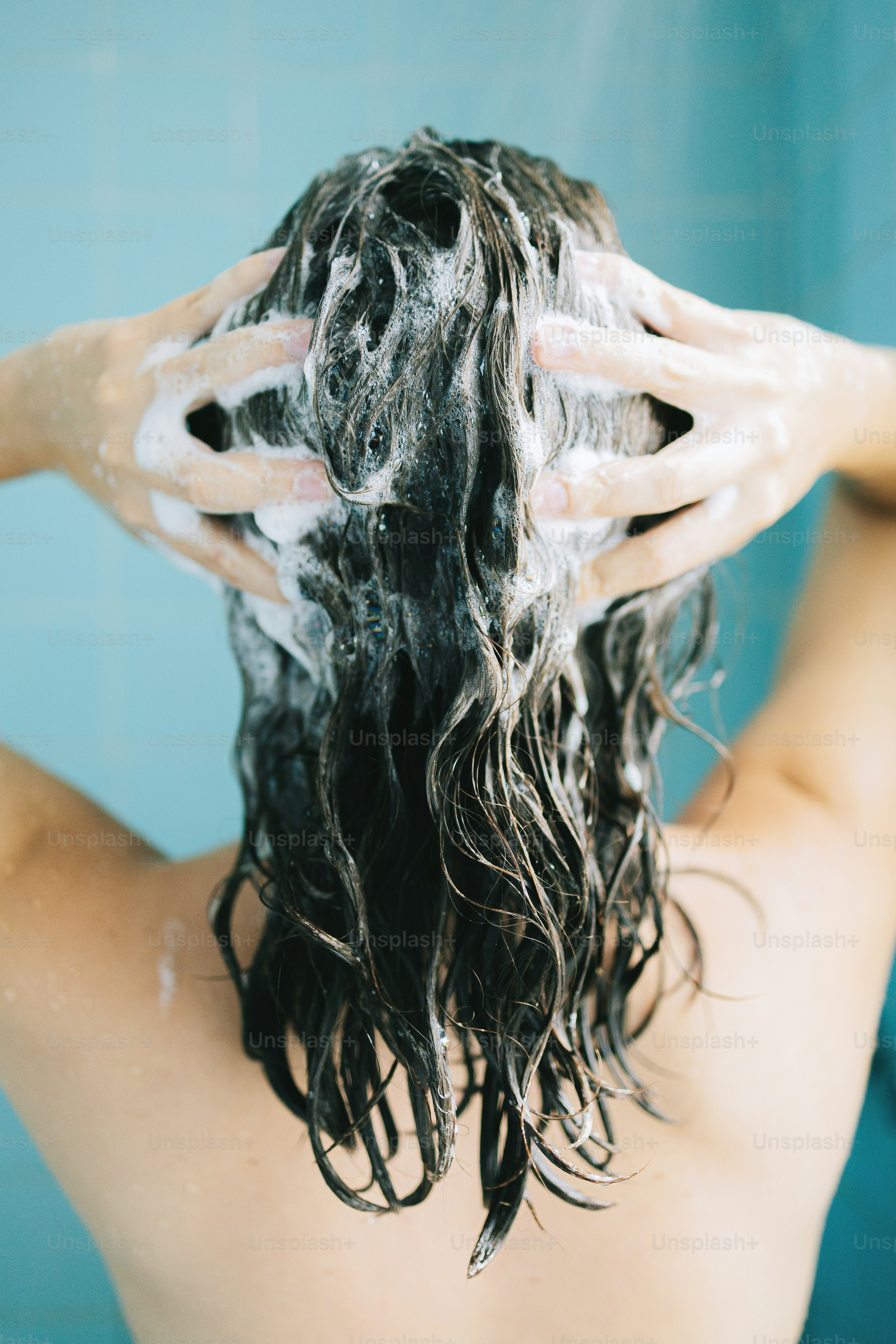 Frau, die sich unter der Dusche die Haare mit Shampoo wäscht