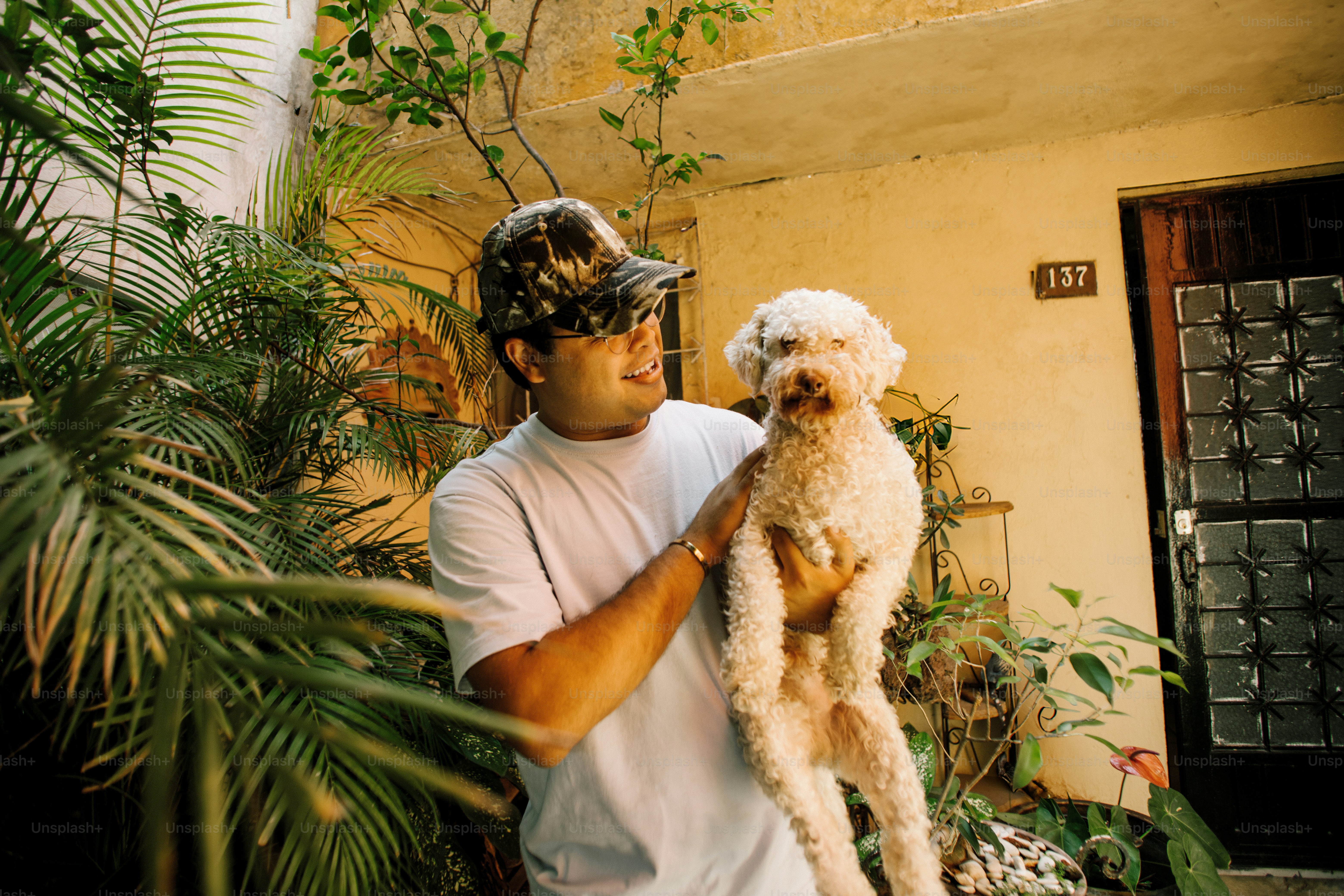 Man holding a small white dog with plants around.