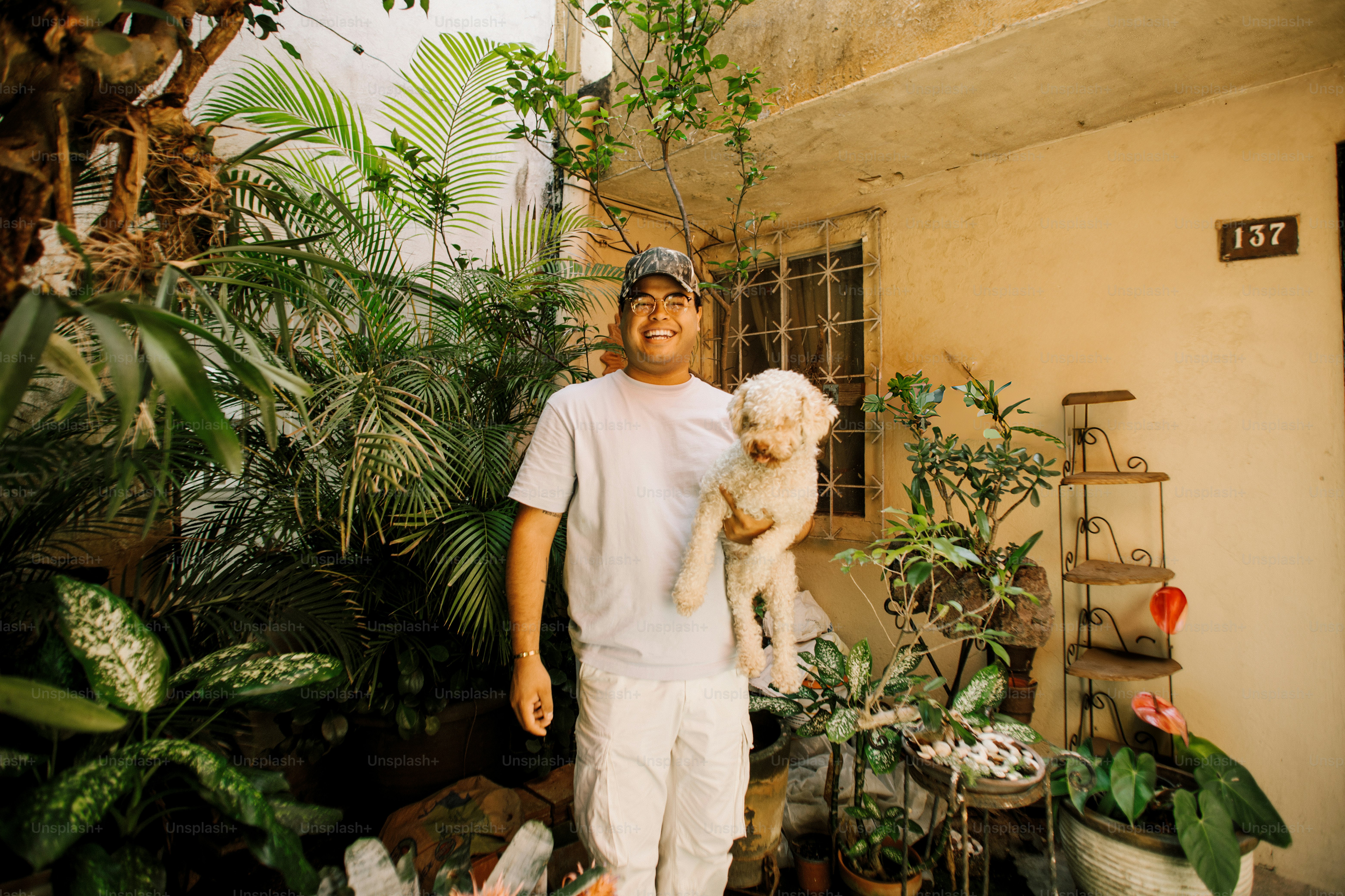 Man holding a small white dog in a lush garden.