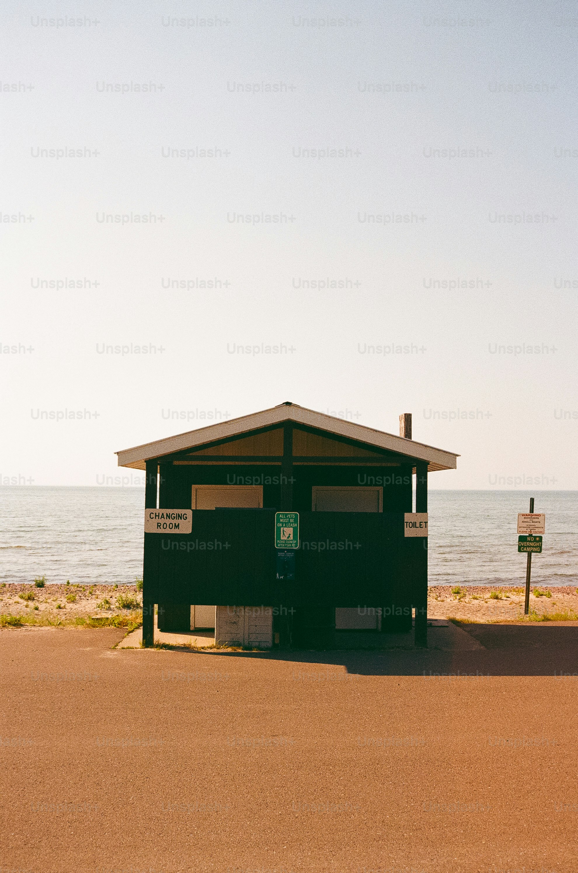 Pequeno edifício escuro em uma praia perto da água.