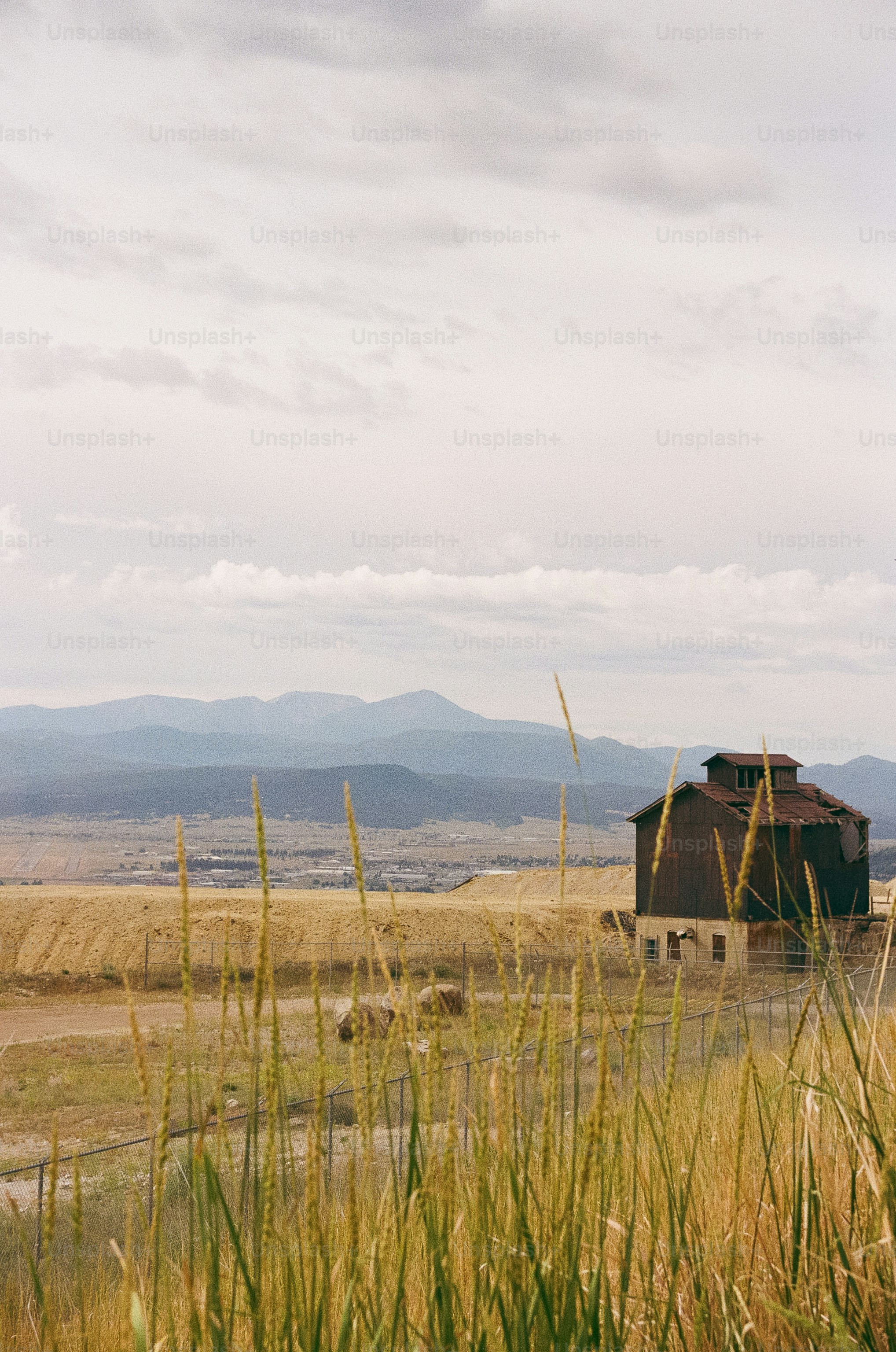Celeiro rústico em uma colina seca e gramada com montanhas.