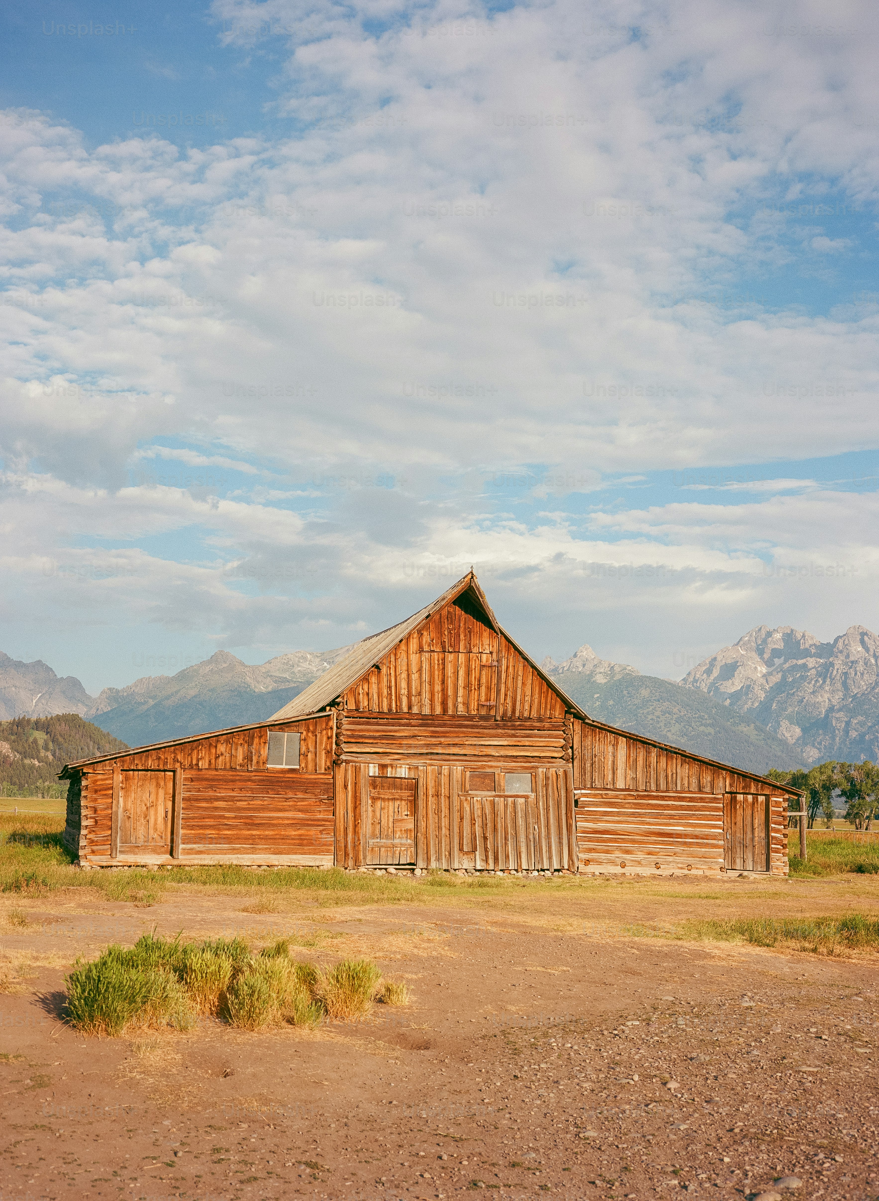 Celeiro de madeira em um campo com montanhas atrás