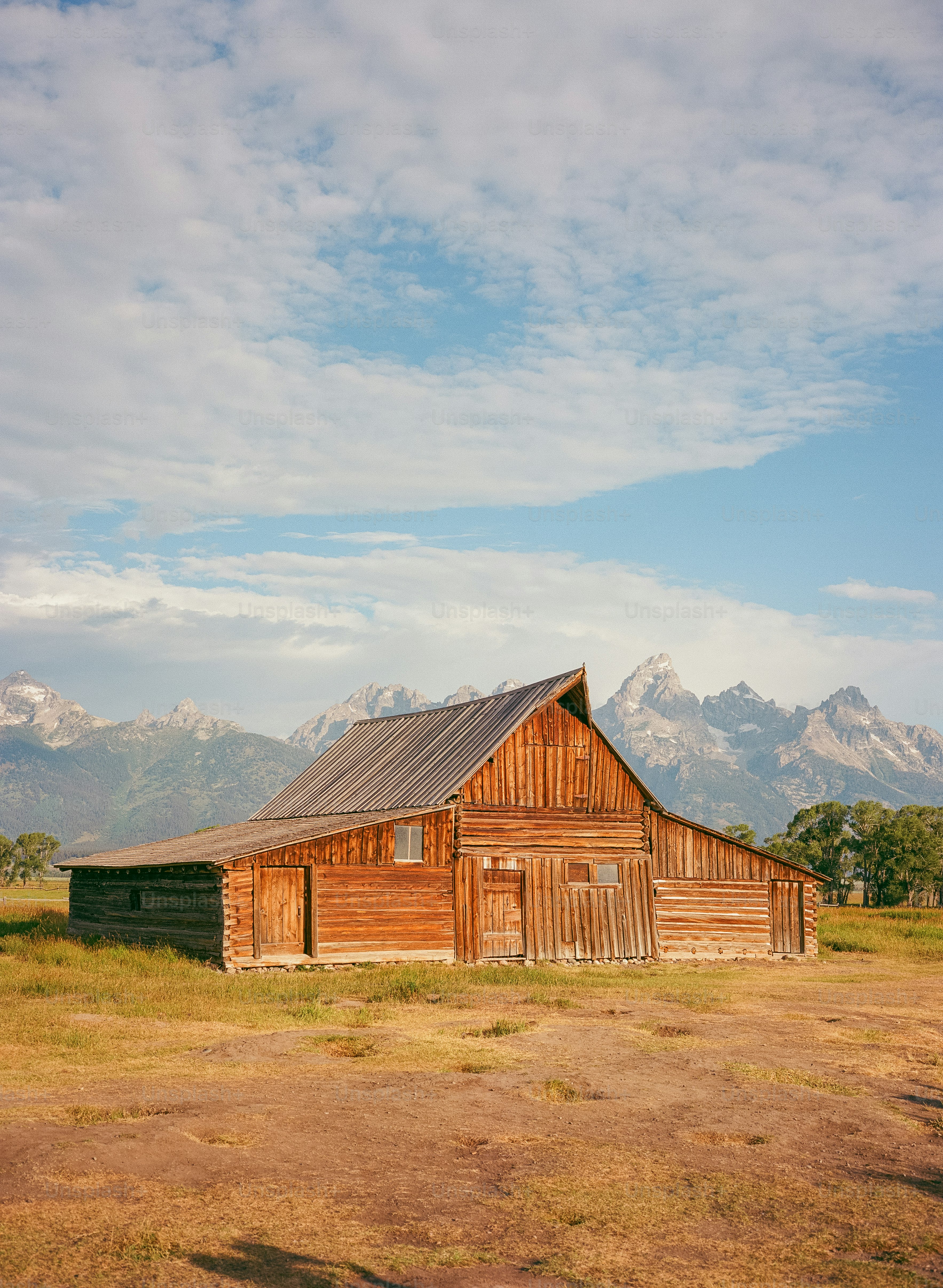 Celeiro de madeira na frente de montanhas majestosas sob o céu nublado