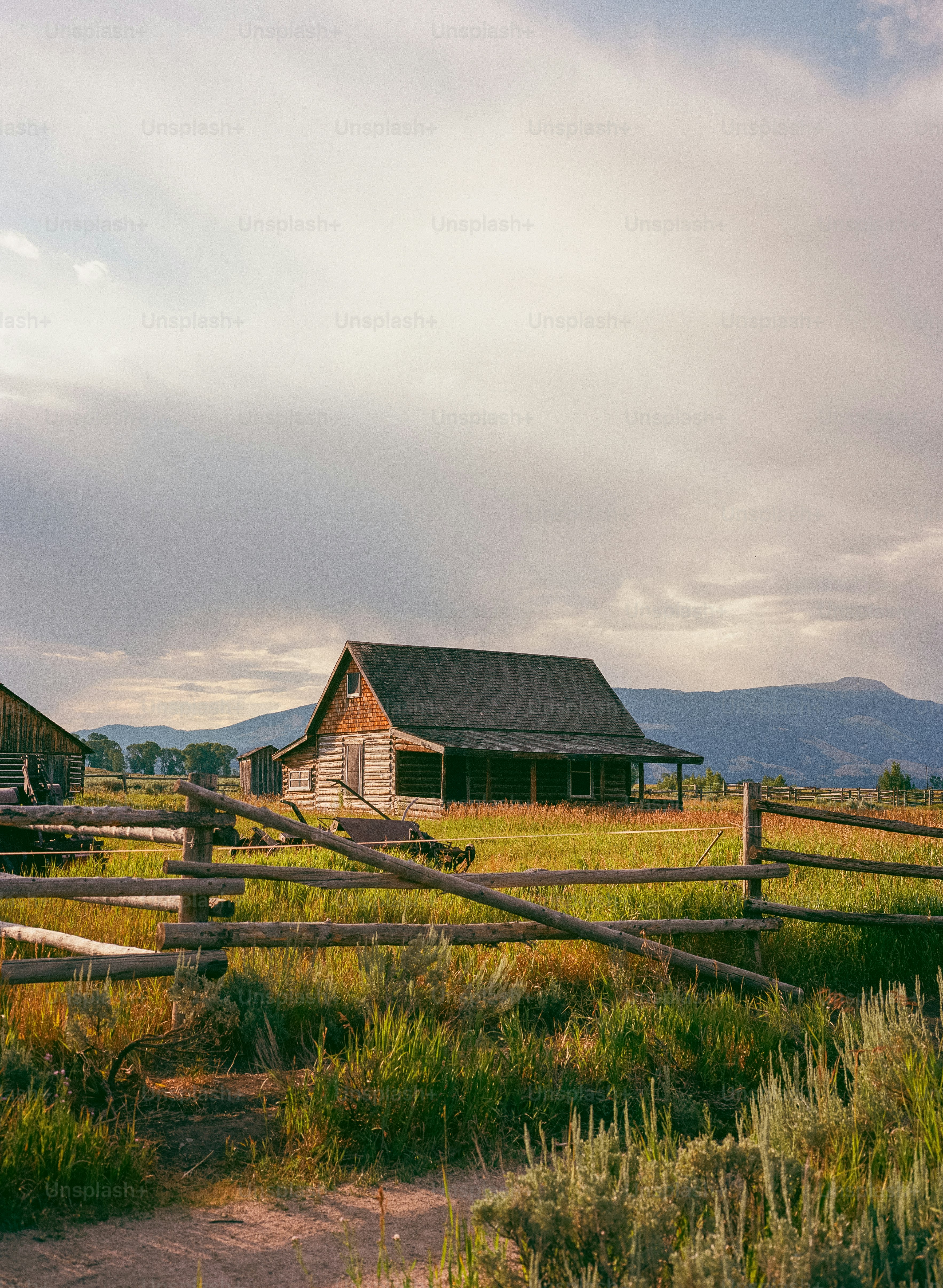 Cabana de madeira rústica atrás de uma cerca desgastada sob o céu nublado.