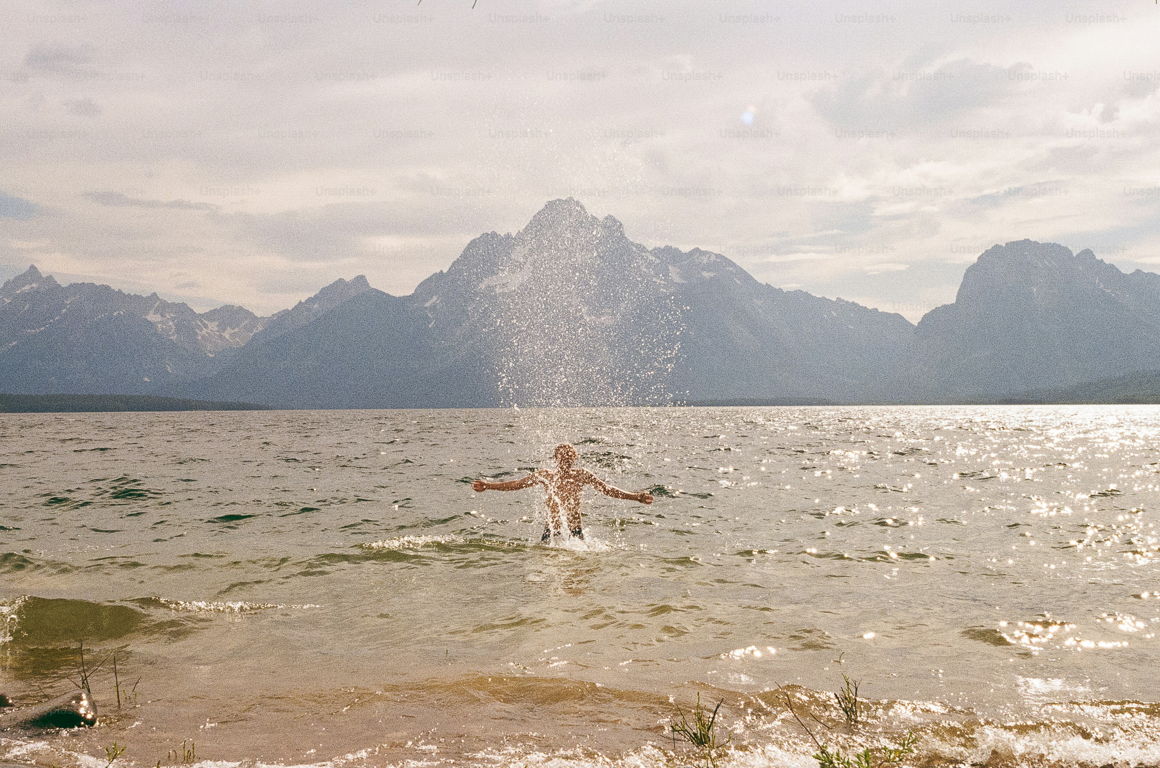 Personne éclaboussant de l’eau dans un lac avec des montagnes derrière.