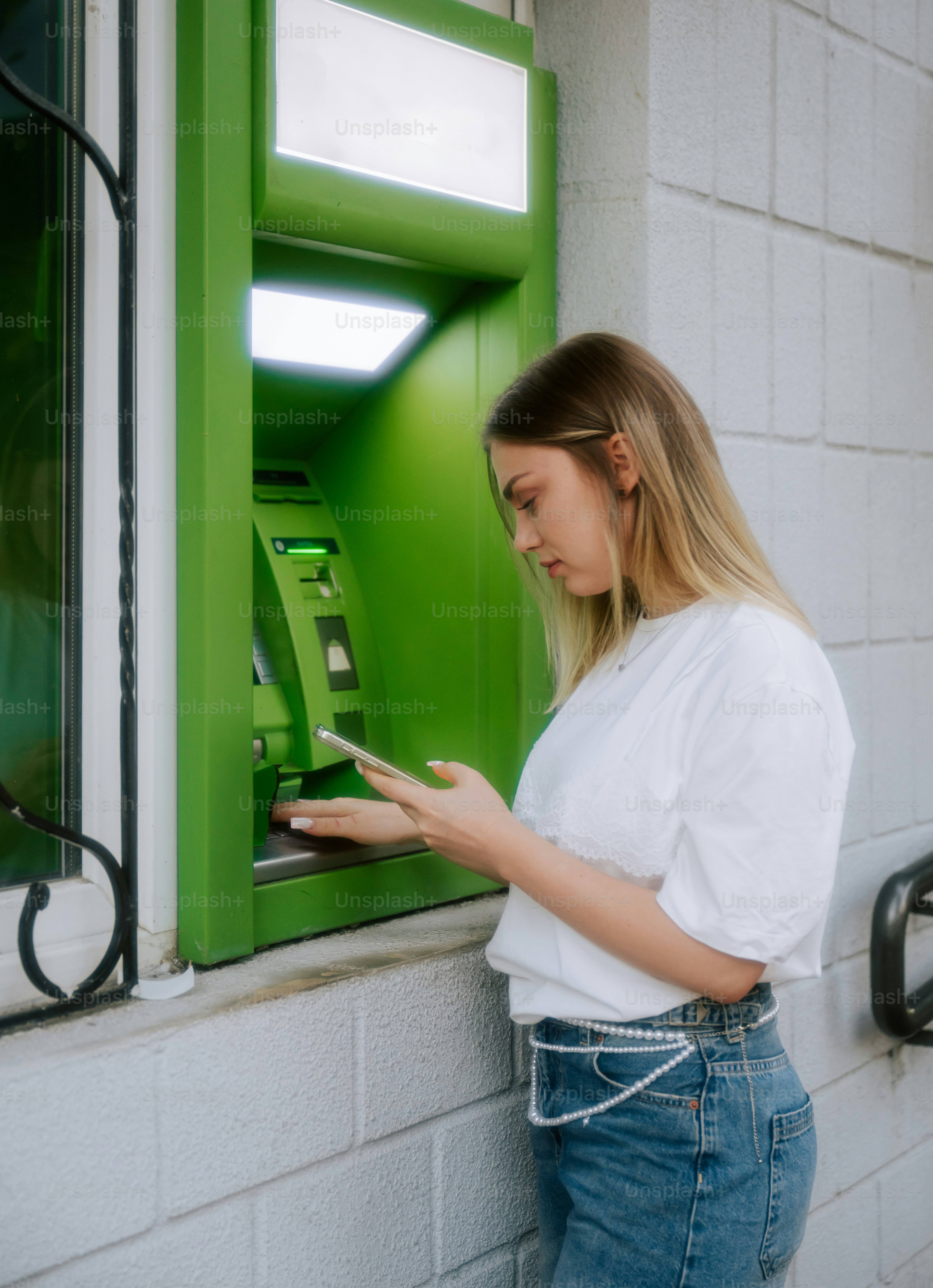 Young woman using smartphone at green atm machine