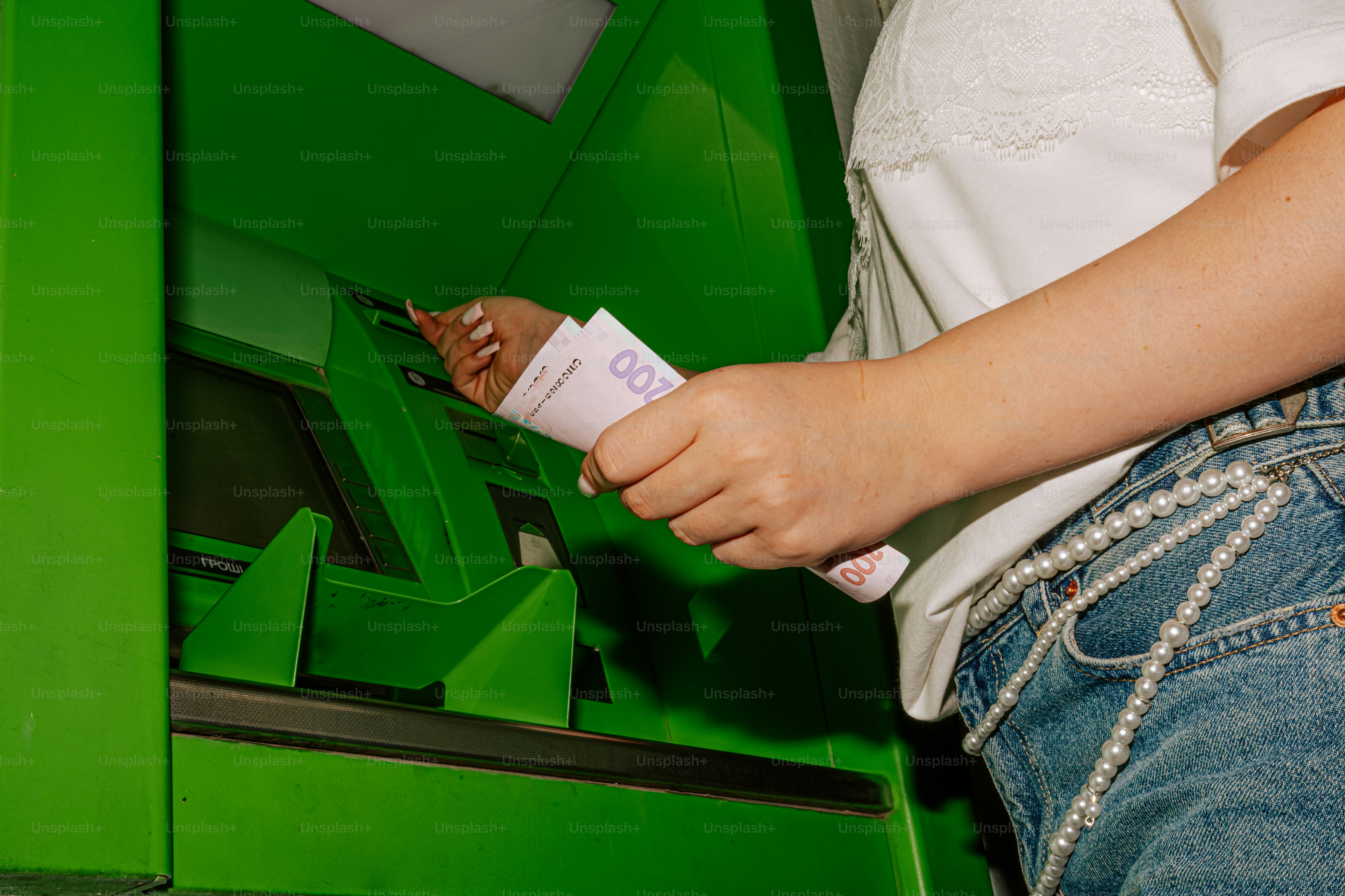 Person withdrawing cash from a green atm.