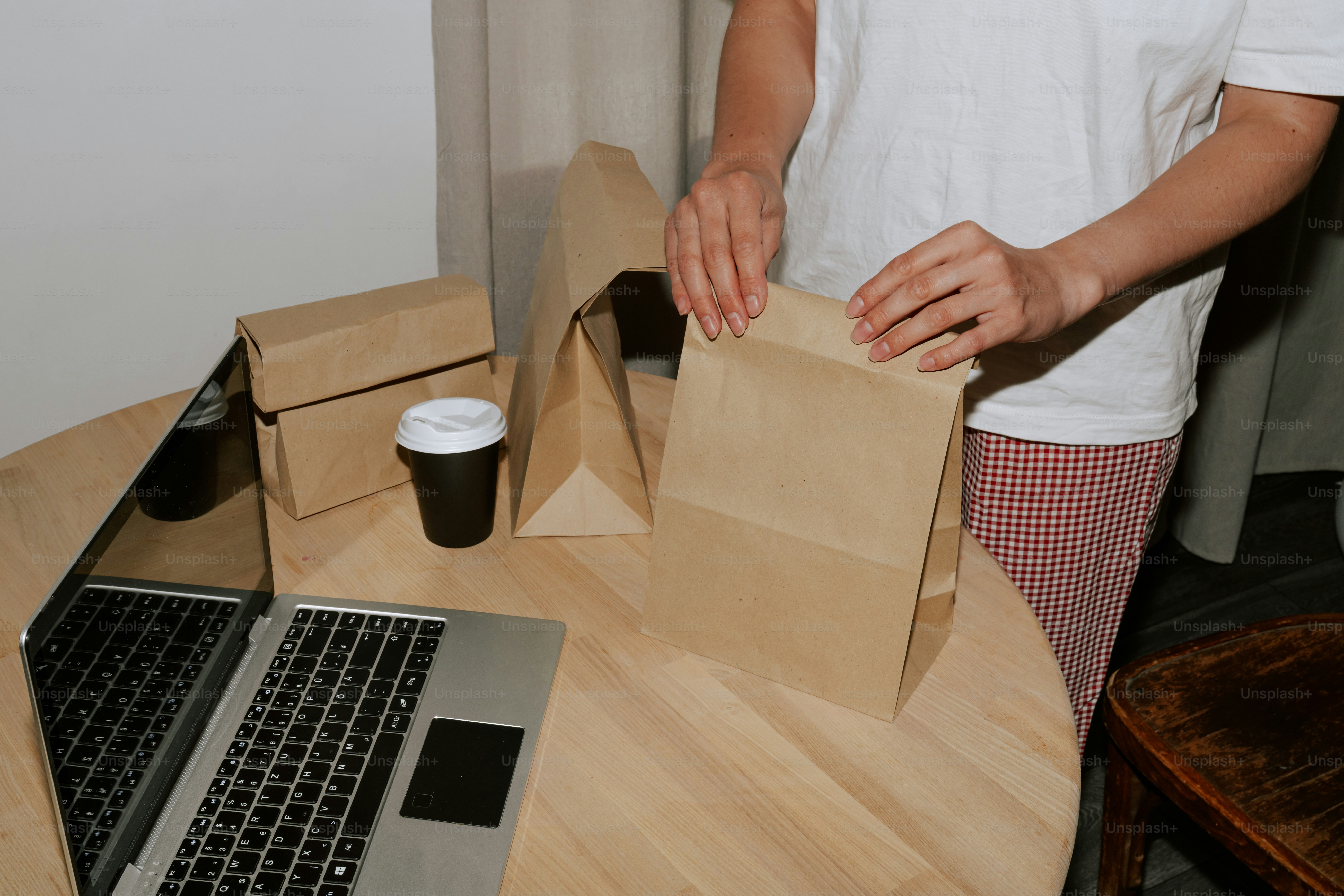 Person packing paper bag next to laptop and coffee.