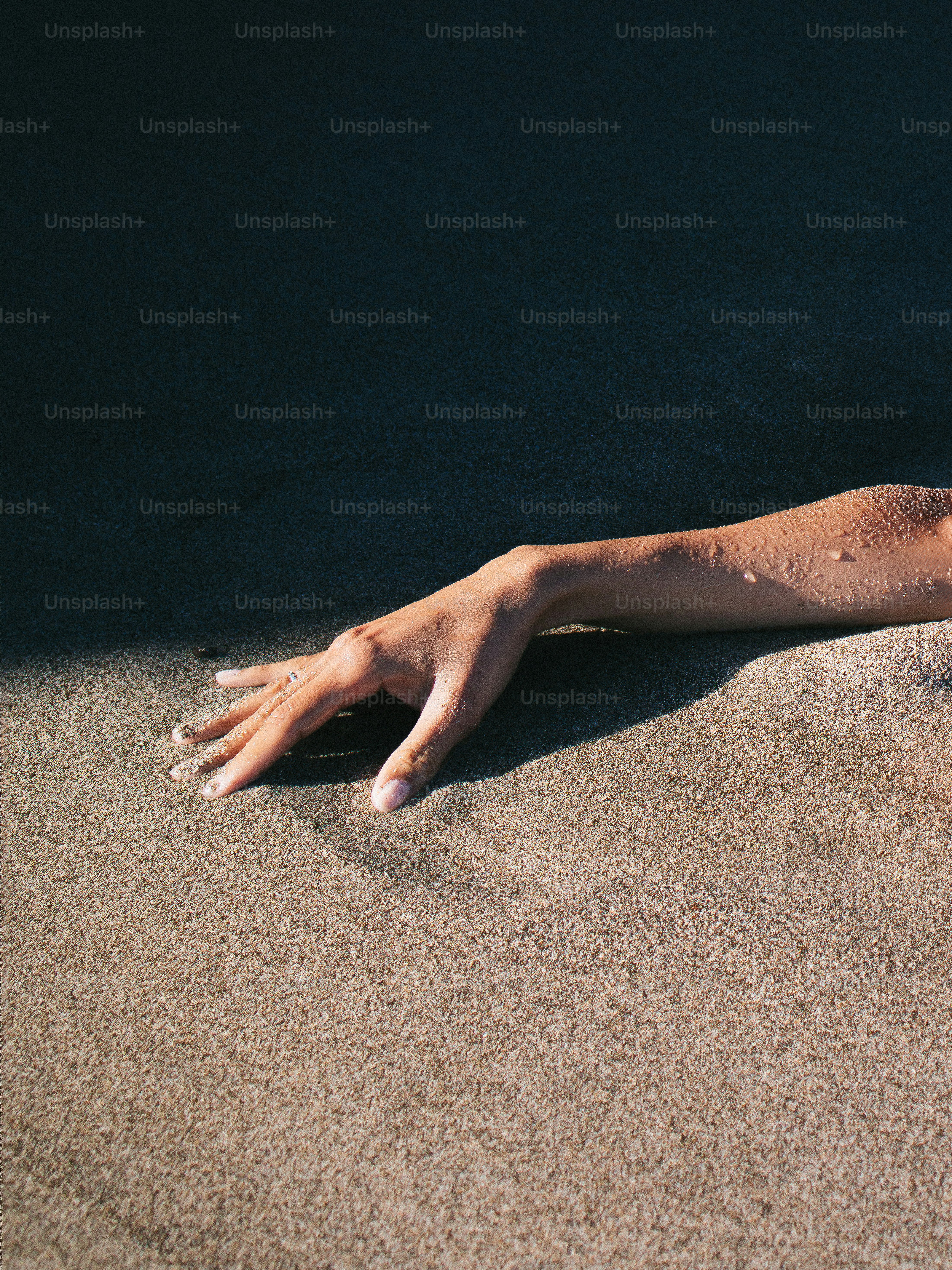Hand emerging from dark sand under sunlight