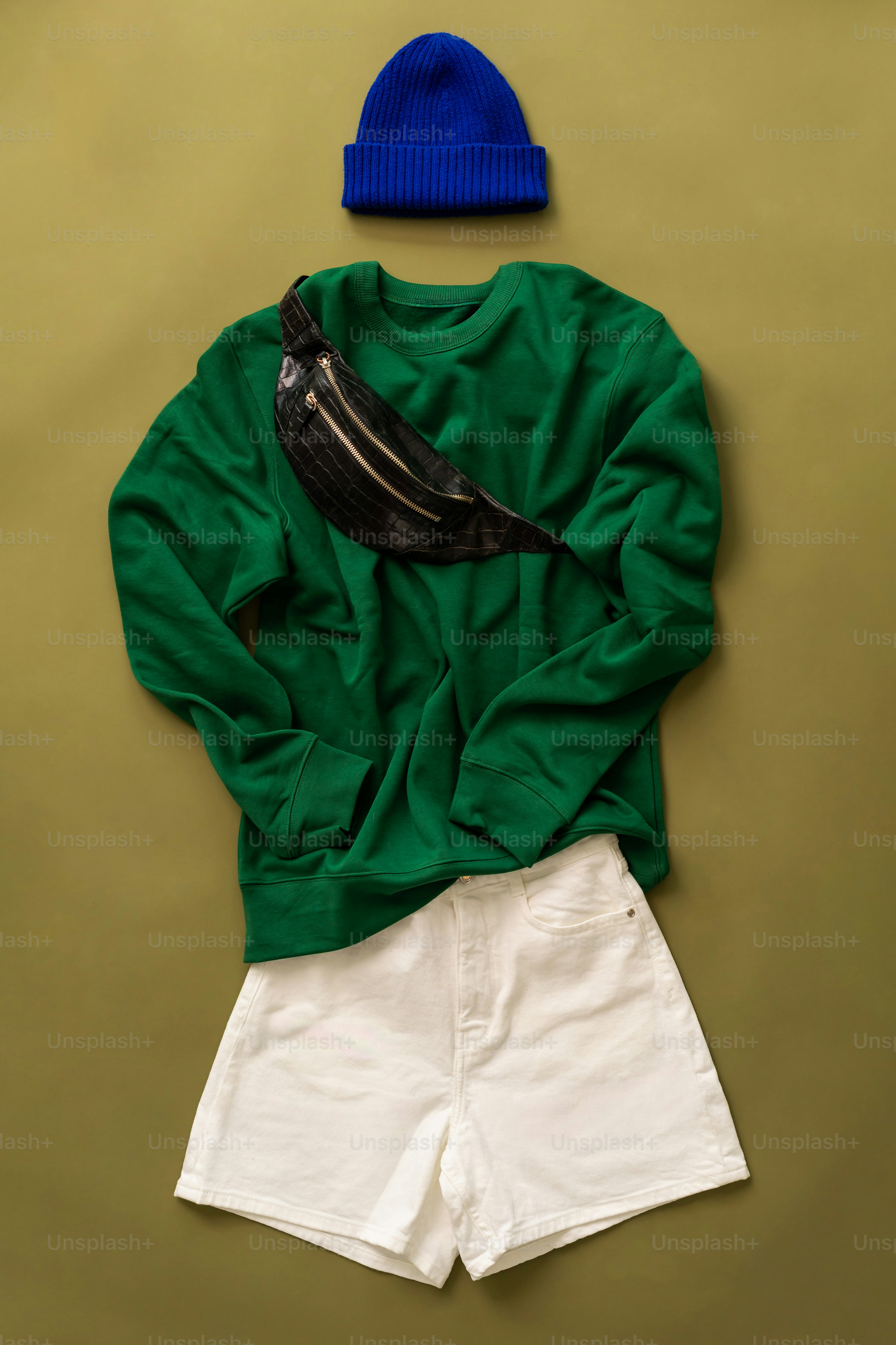 Green sweatshirt, white shorts, and blue beanie with fanny pack.
