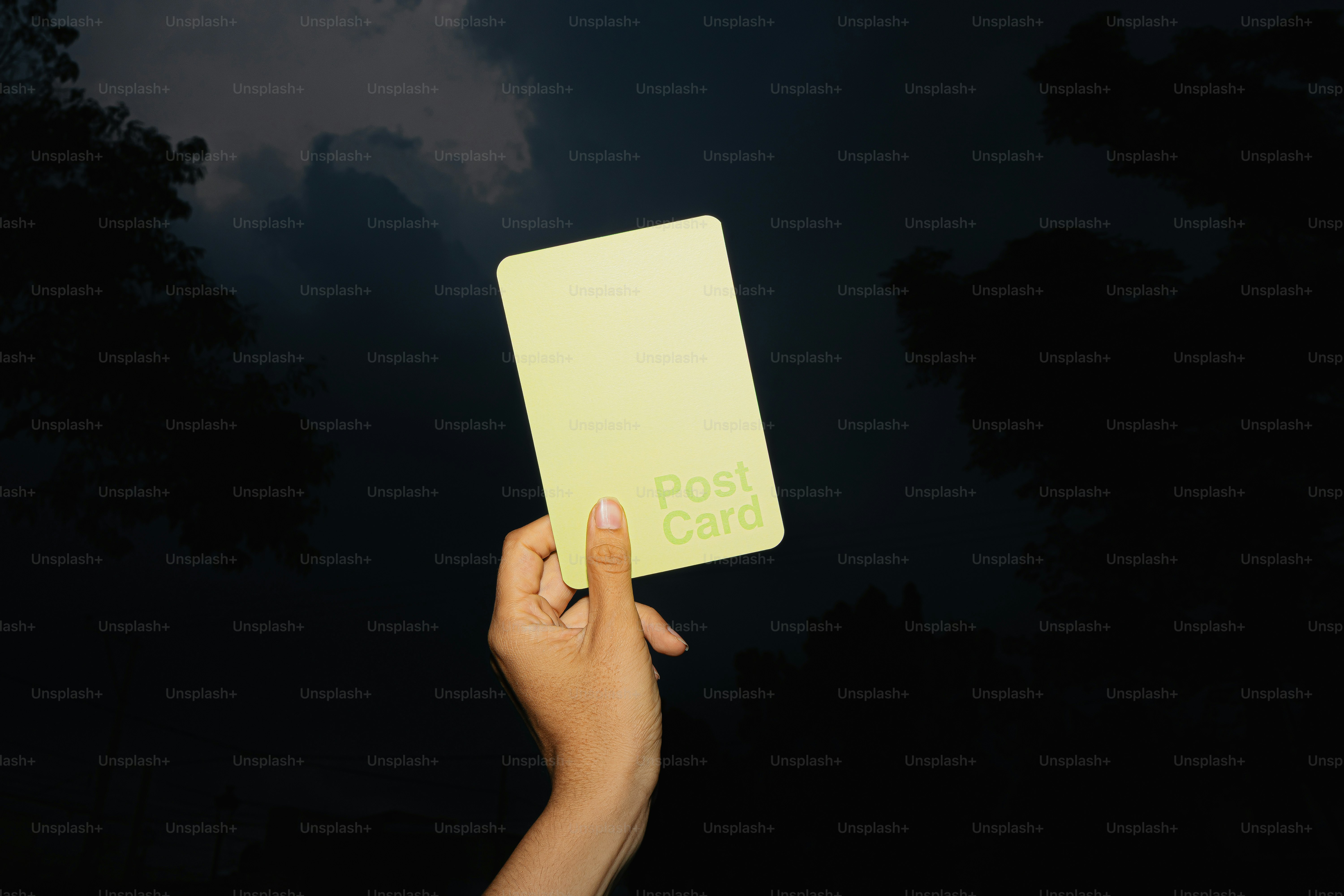 Hand holding a yellow postcard against dark background