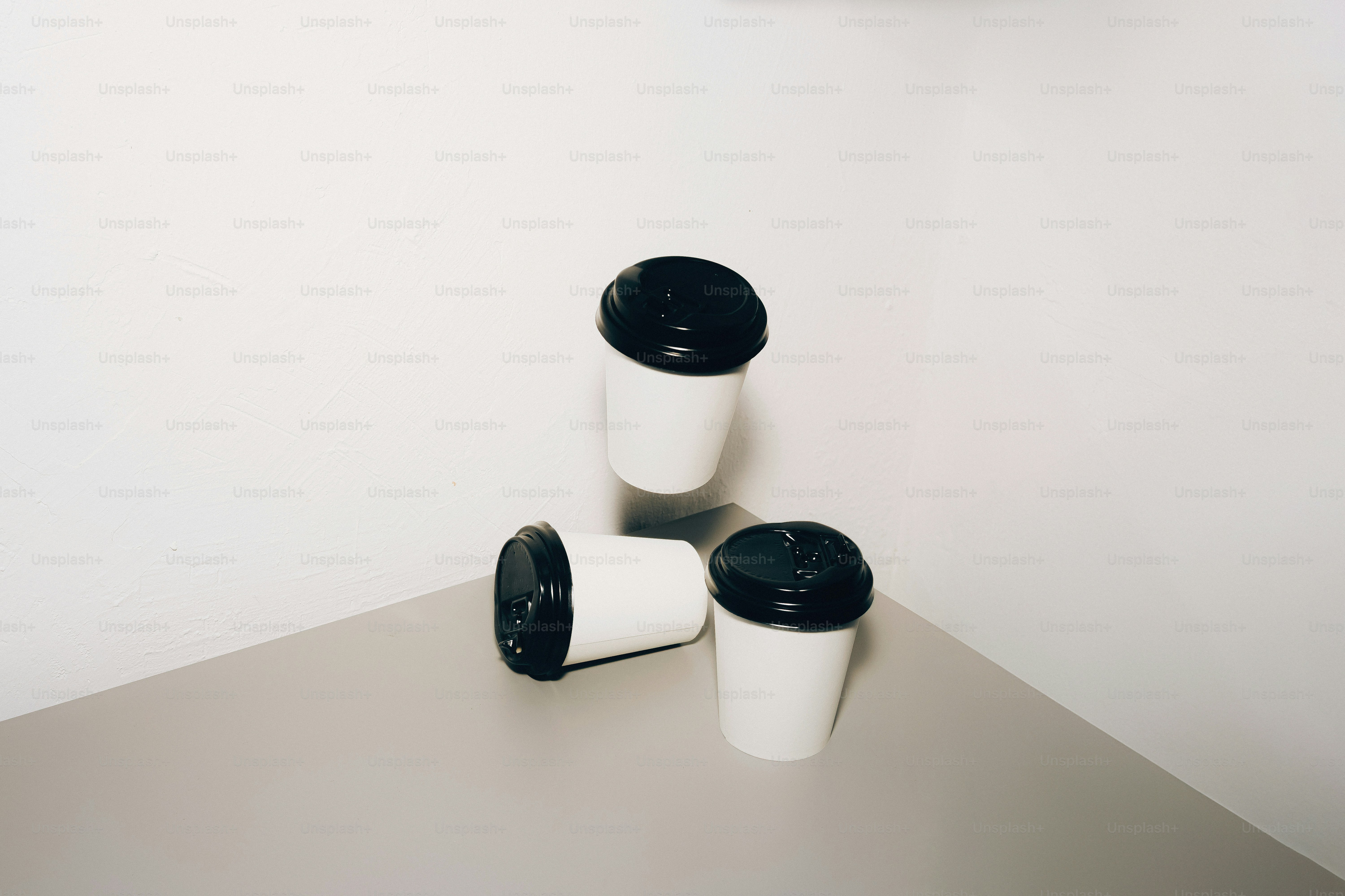 Three white coffee cups with black lids on table.