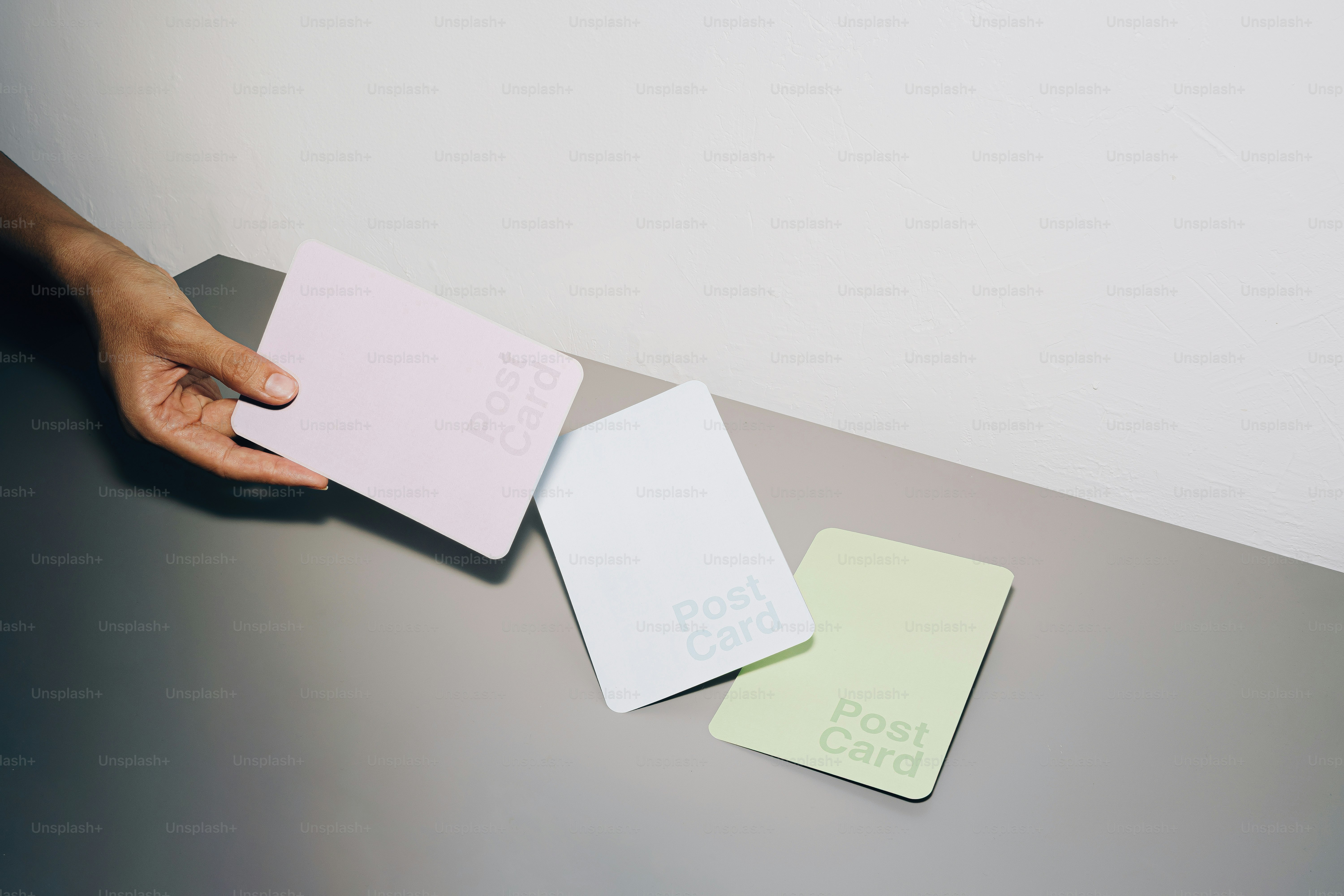 Hand holding pastel postcards on a gray surface