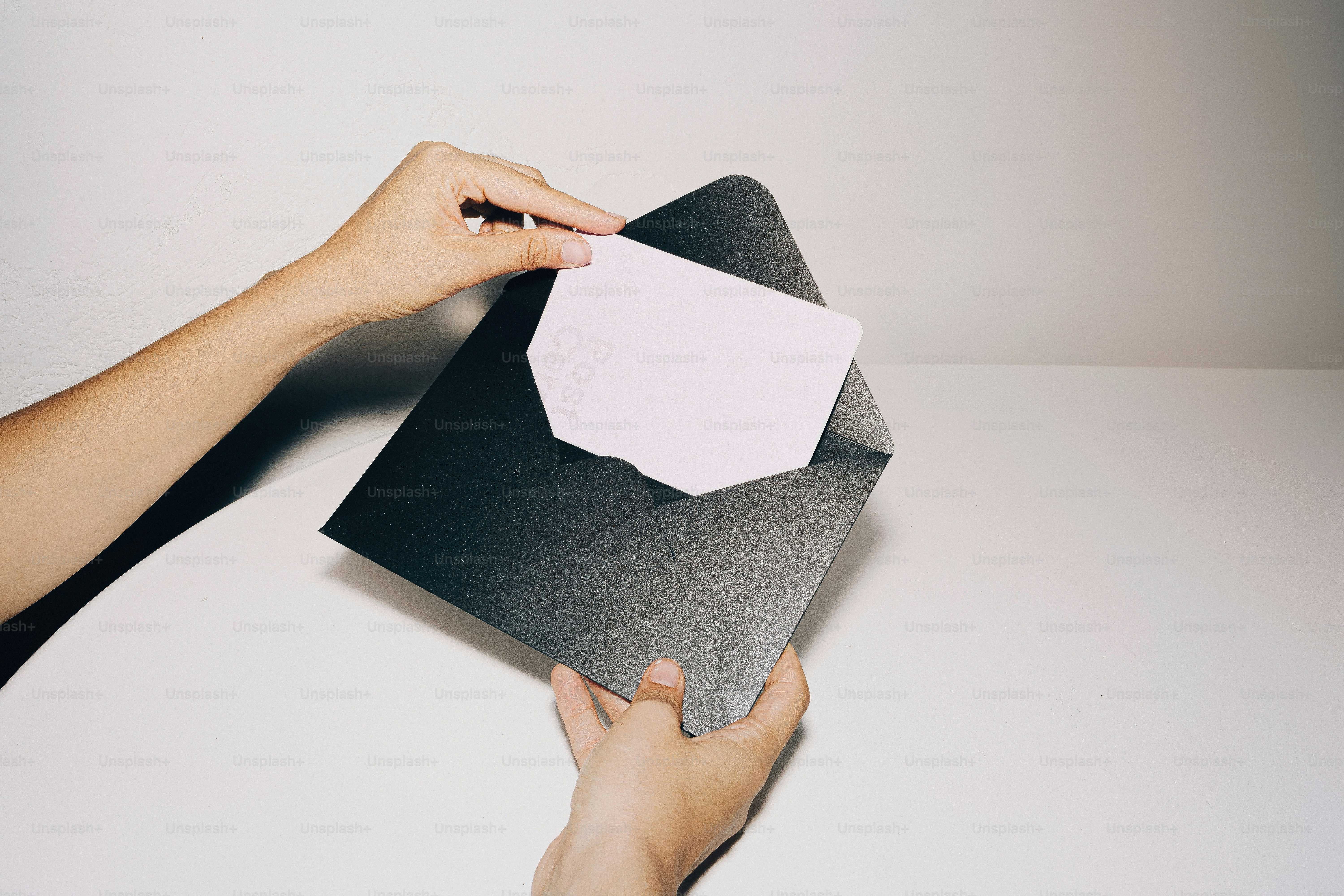 Hands opening a black envelope with a white card.