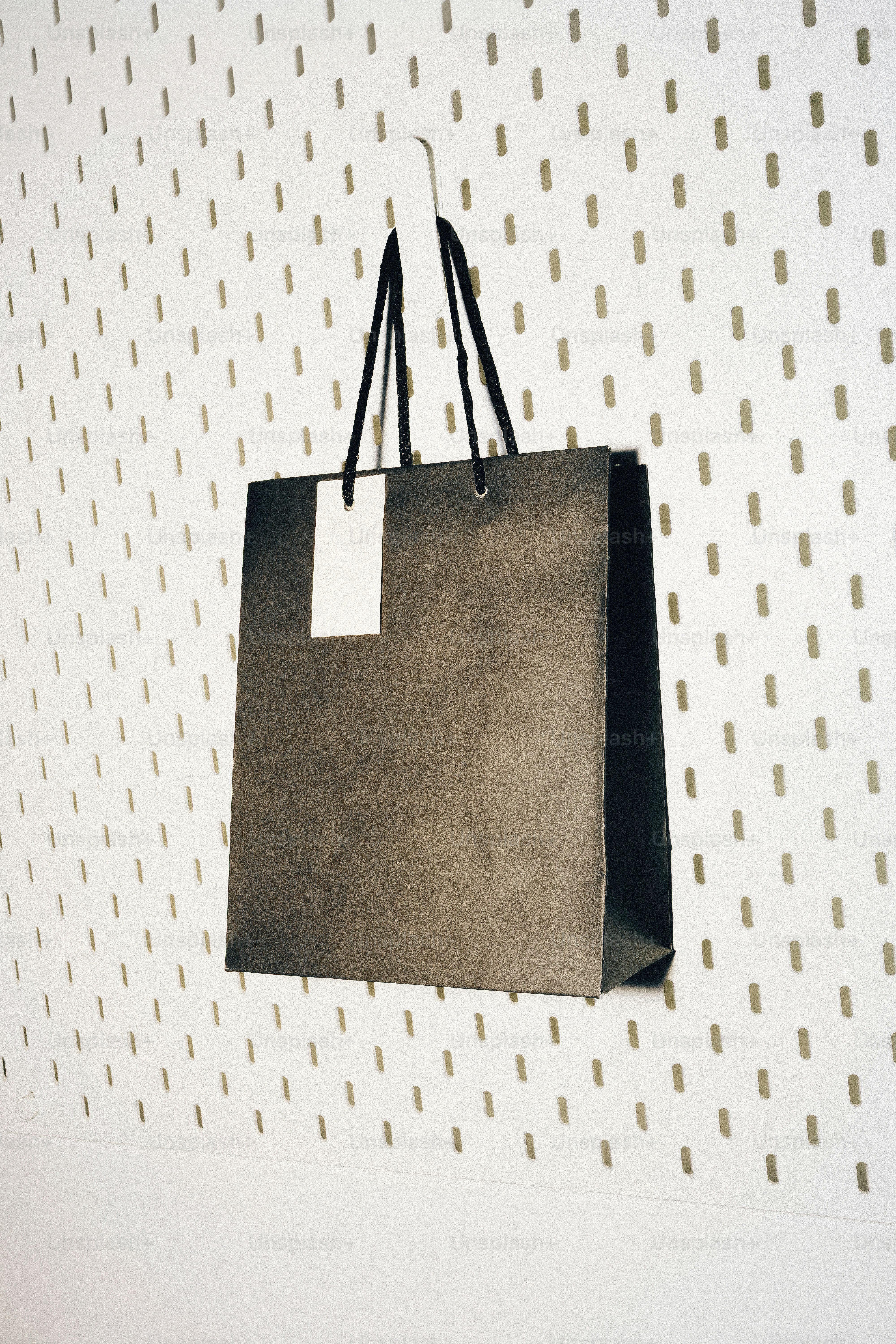 Black shopping bag hanging on a pegboard wall.