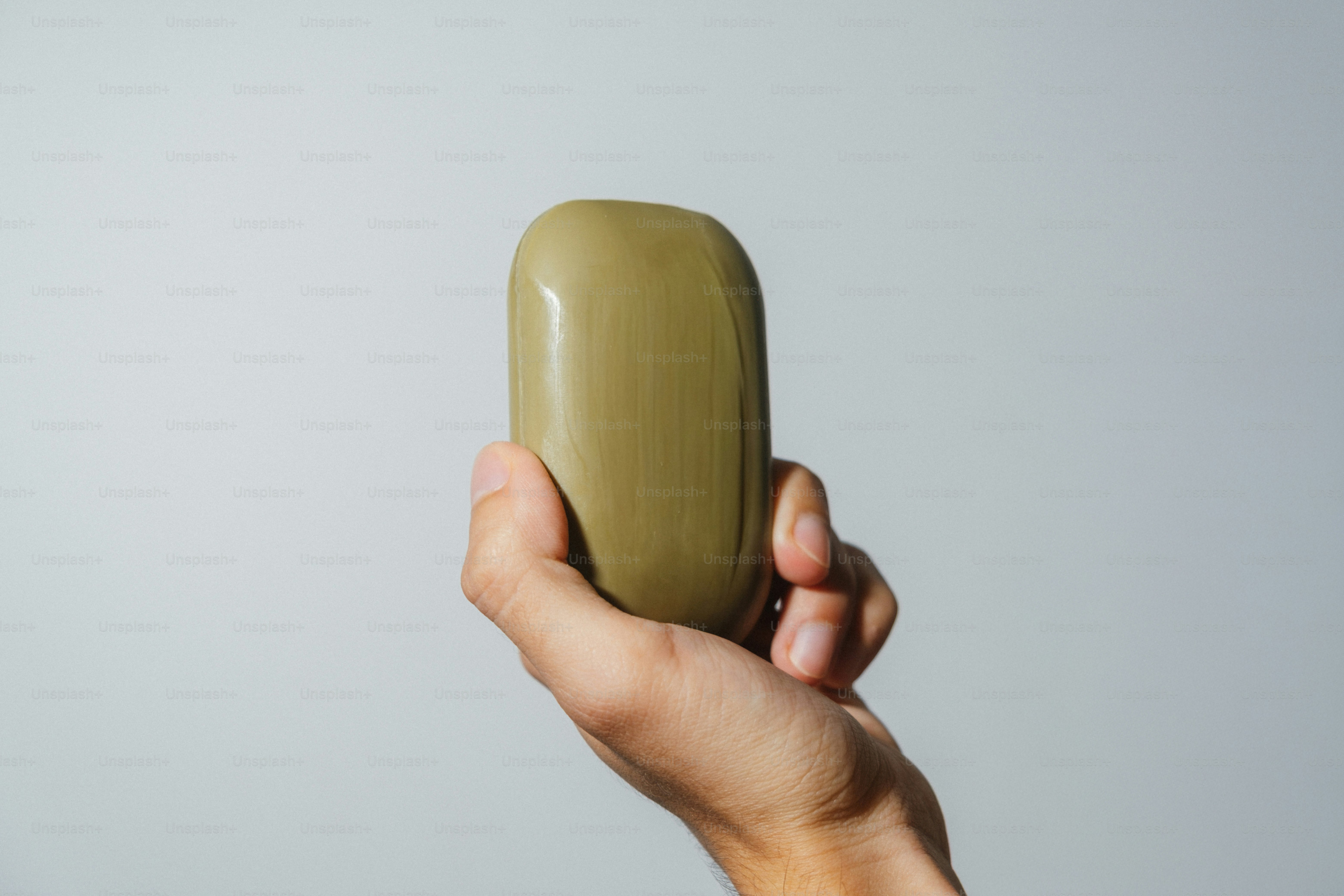 Hand holding a smooth, olive-green bar of soap.