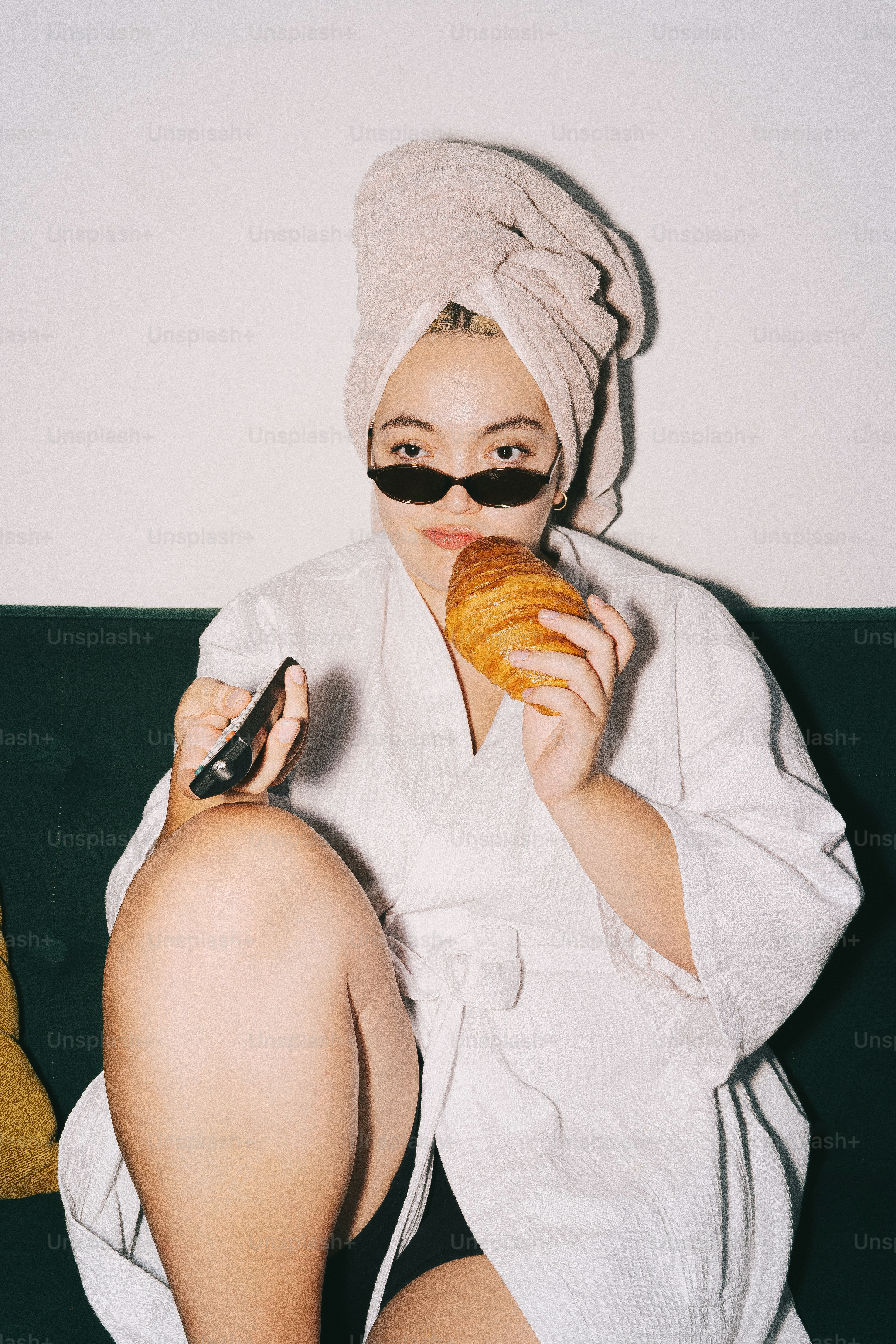 Woman in robe eats croissant, holds phone