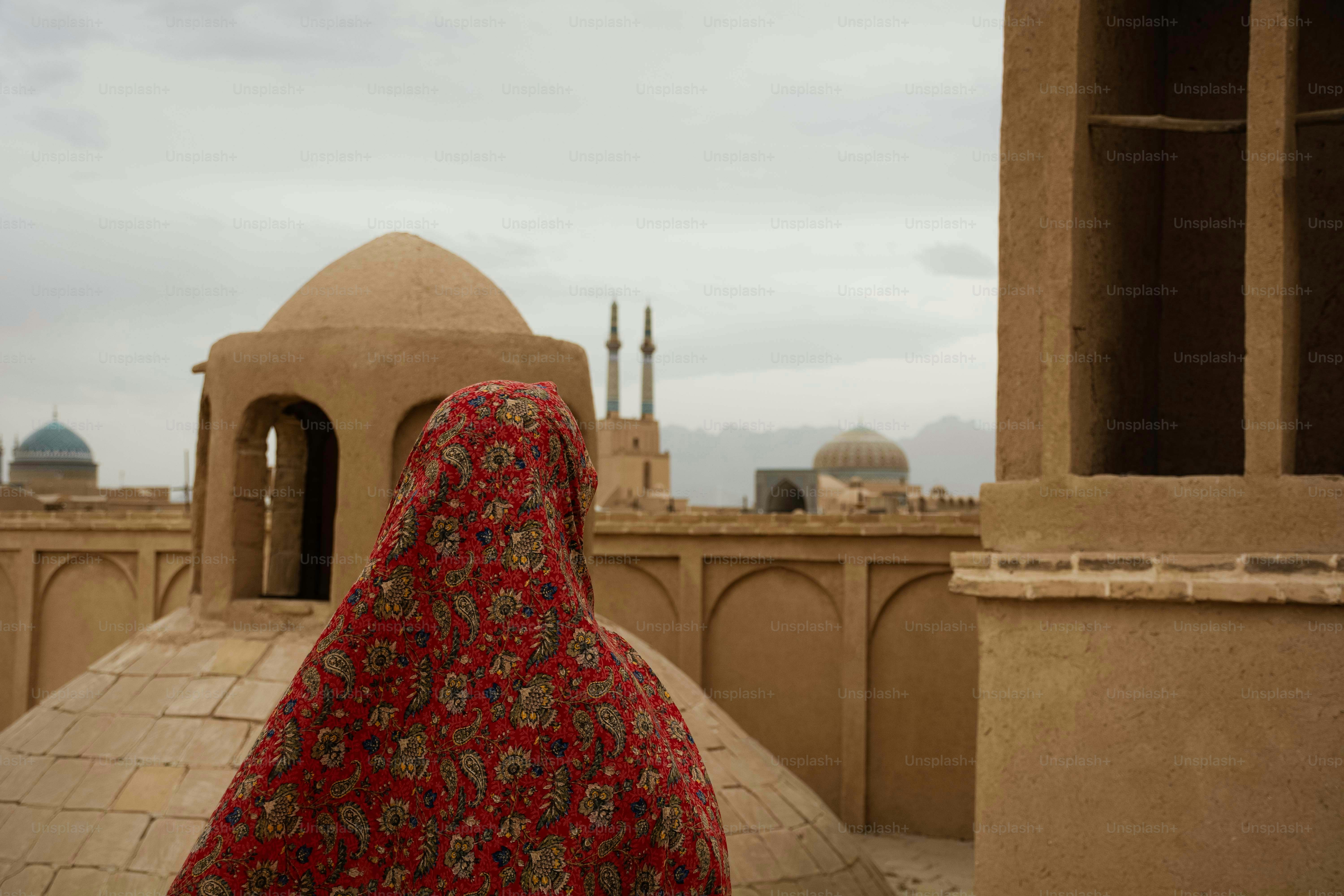 Woman in red veil overlooks desert city rooftops
