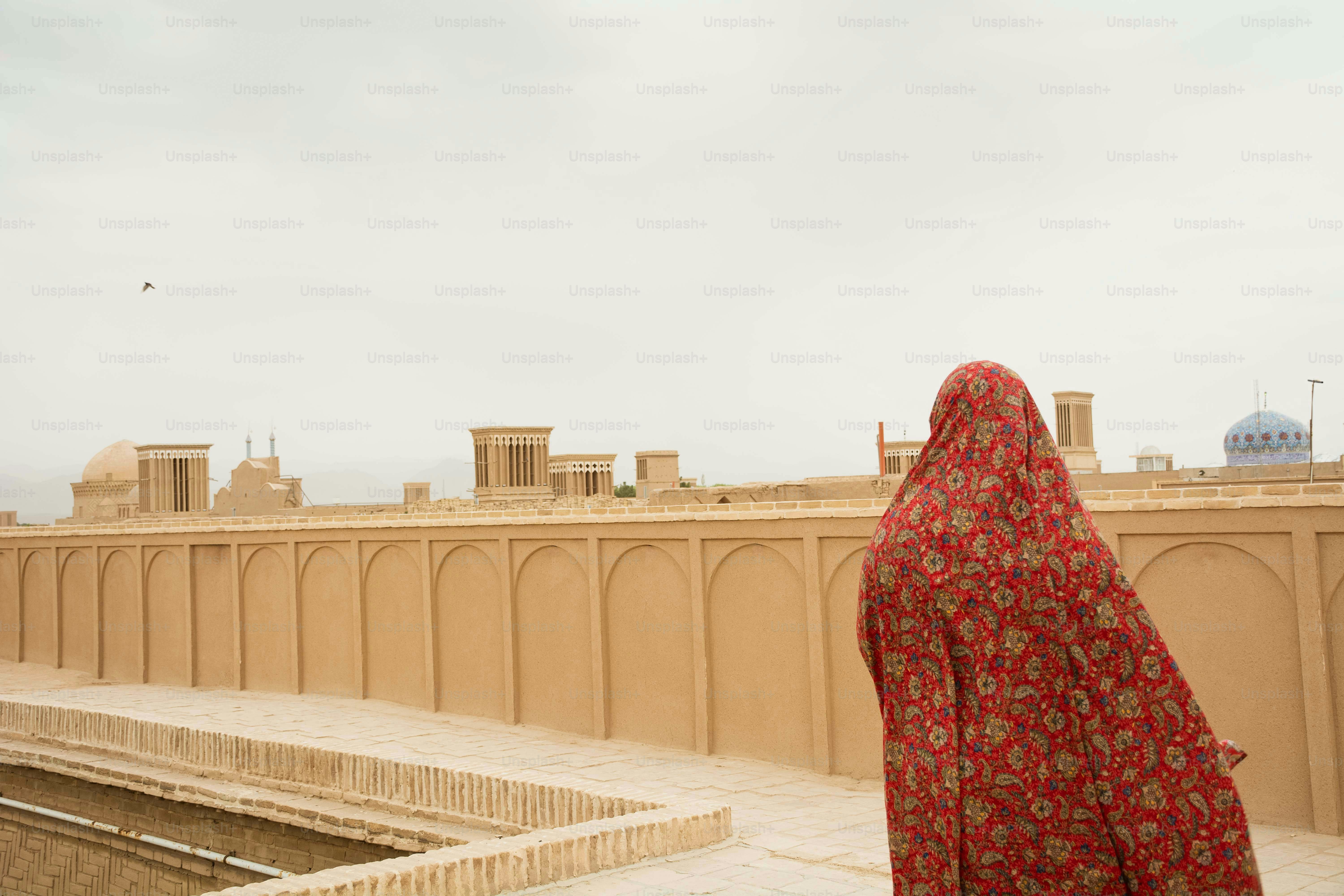 Woman in red hijab overlooks desert city architecture