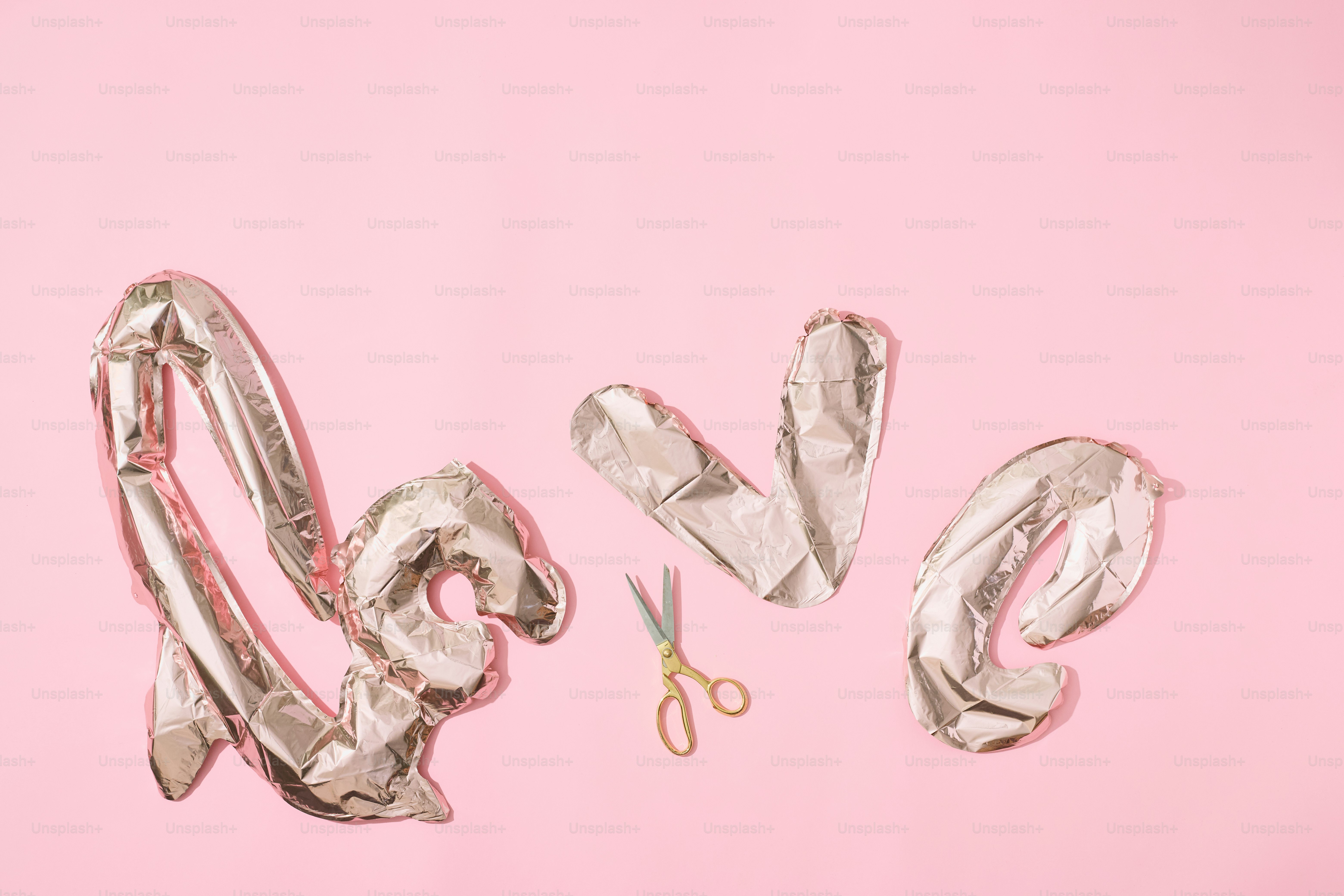 Des ballons argentés épellent l’amour avec des ciseaux sur fond rose