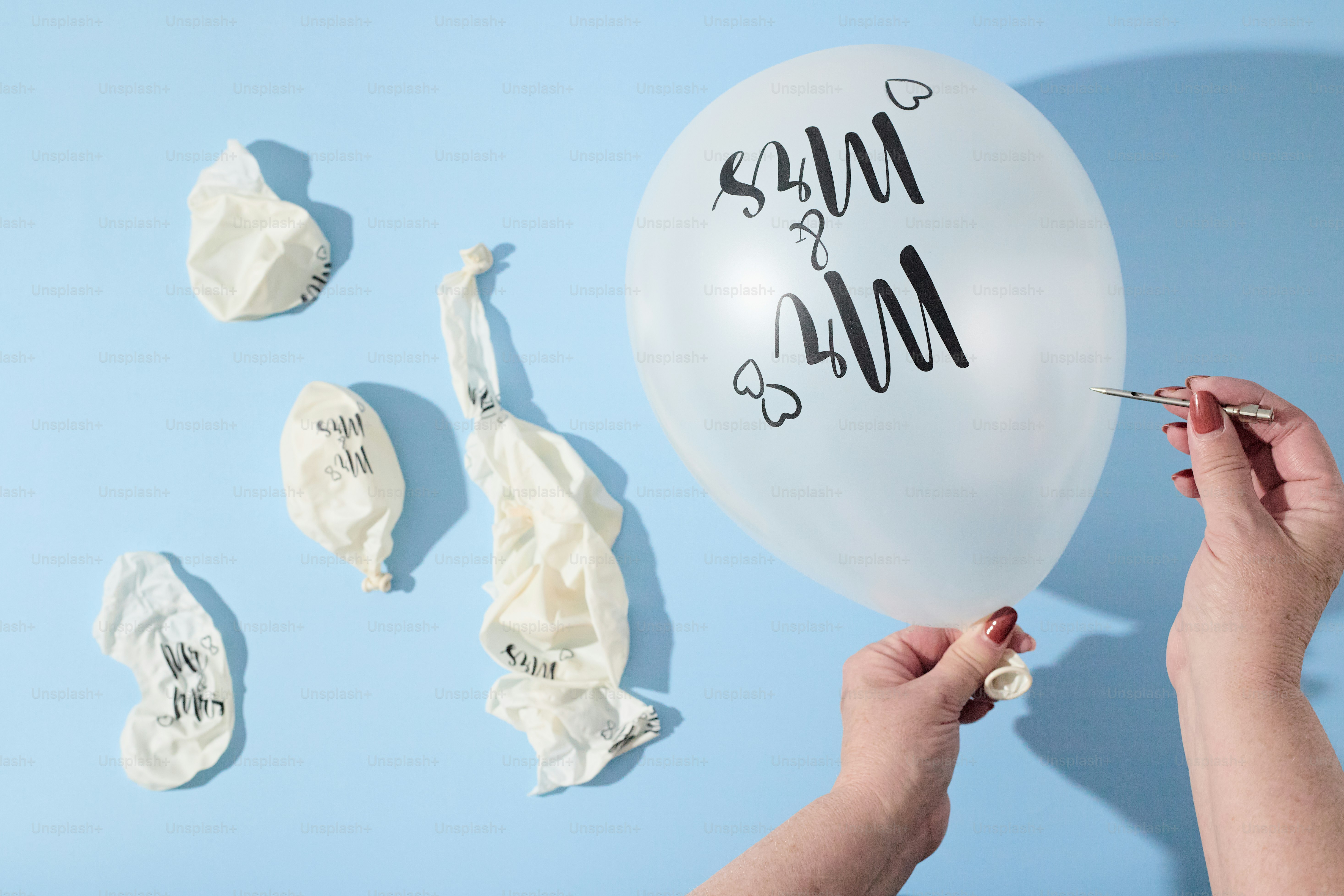 Hände, die einen Luftballon mit einer Stecknadel auf blauem Hintergrund platzen lassen