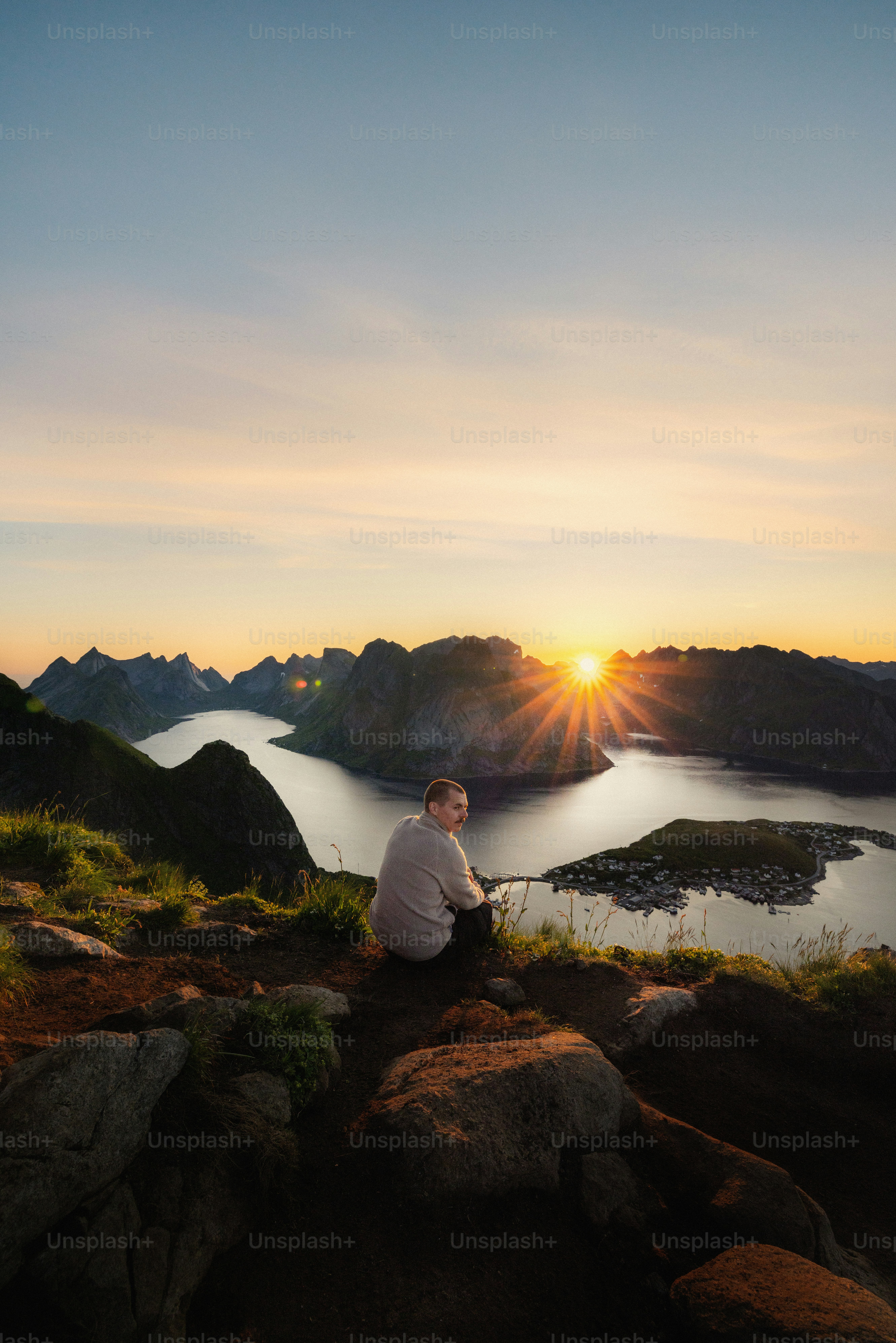 Man sitting on mountain overlooking village at sunset