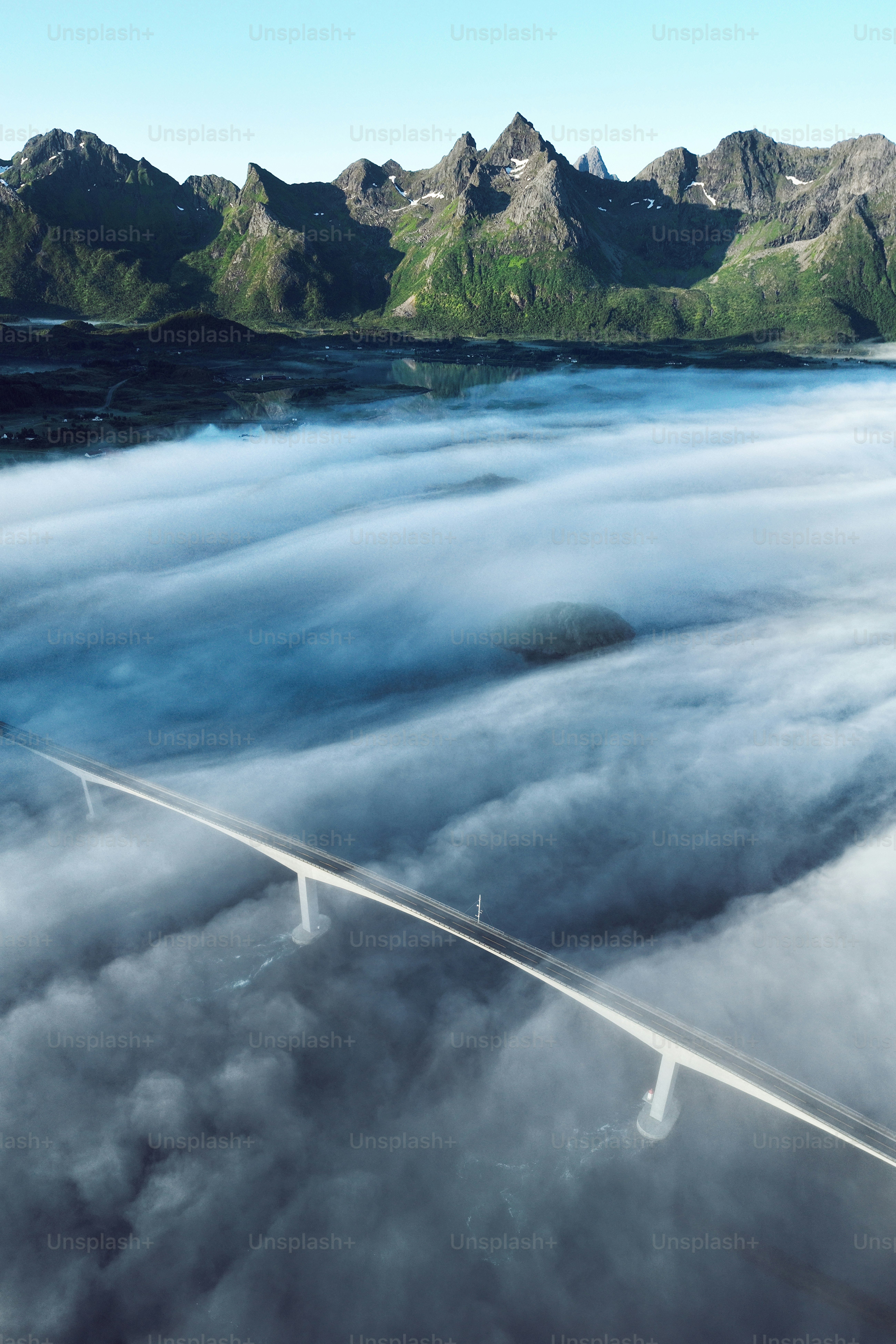 Modern bridge emerges from sea fog towards mountains.