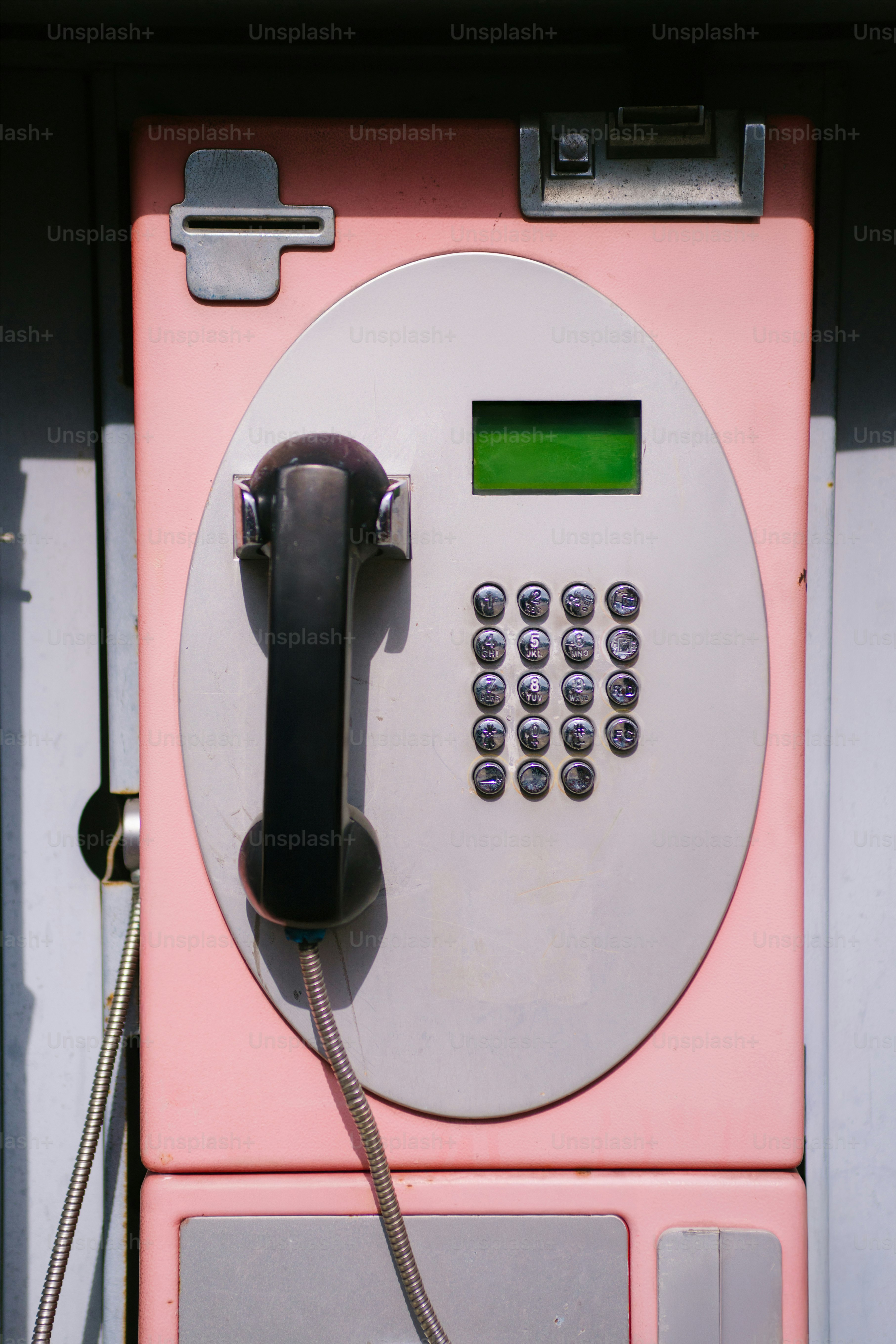 Um telefone público rosa com um aparelho preto.
